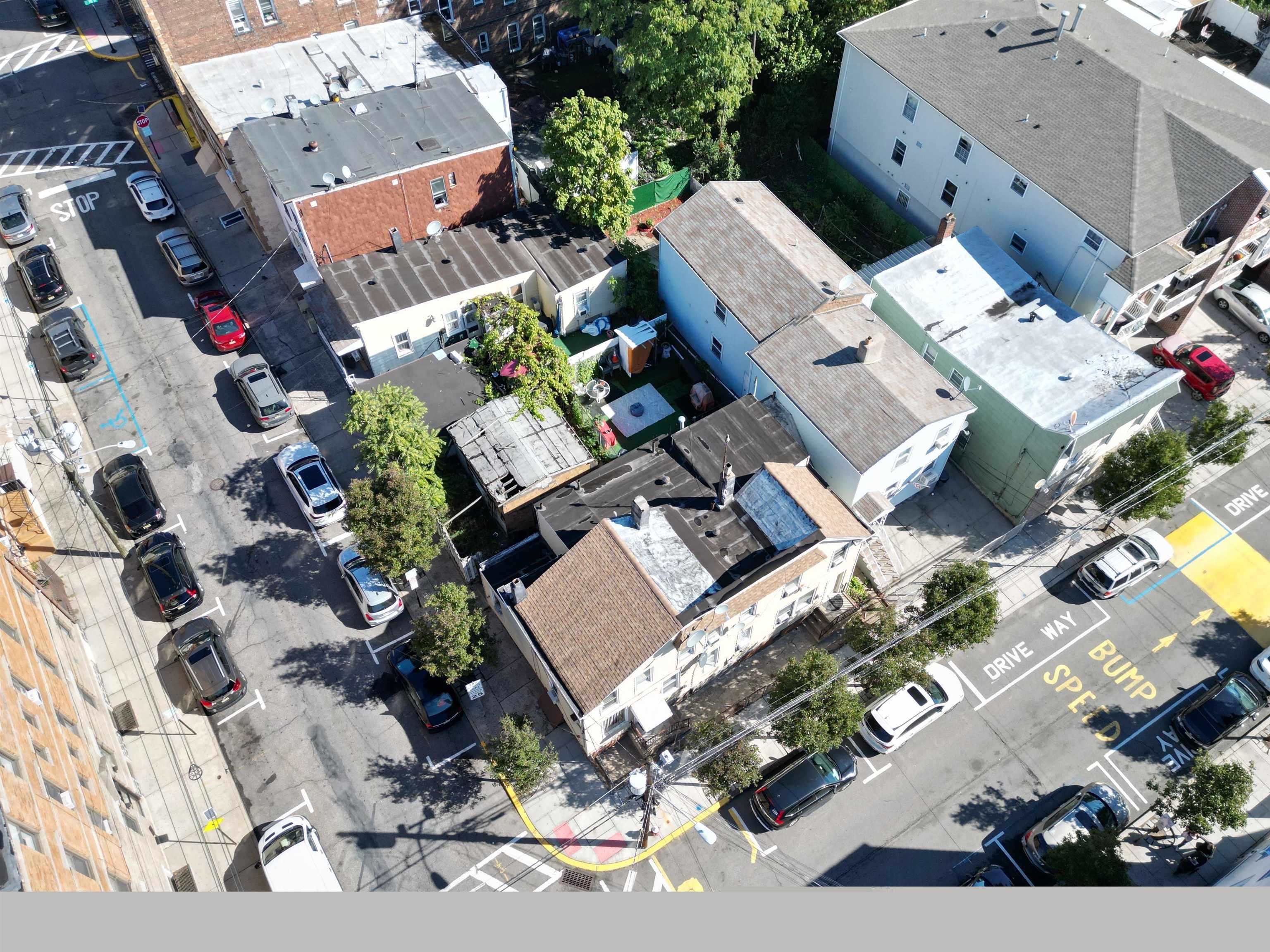 Aerial view of a residential block with closely spaced homes, leafy yards, and parked cars.