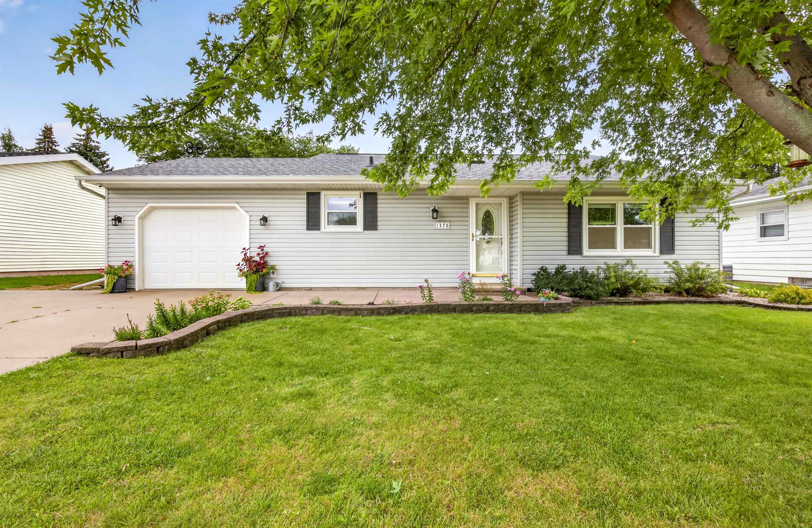 Single-story gray house with a garage, leafy shade trees, and a landscaped front lawn.