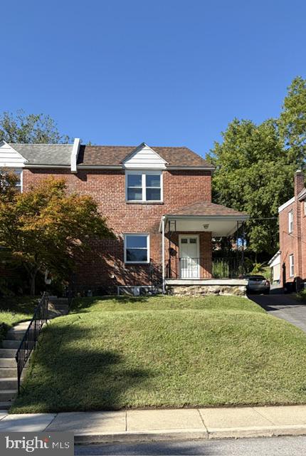 Two-story red-brick home with a covered entrance, sloped lawn, and driveway.