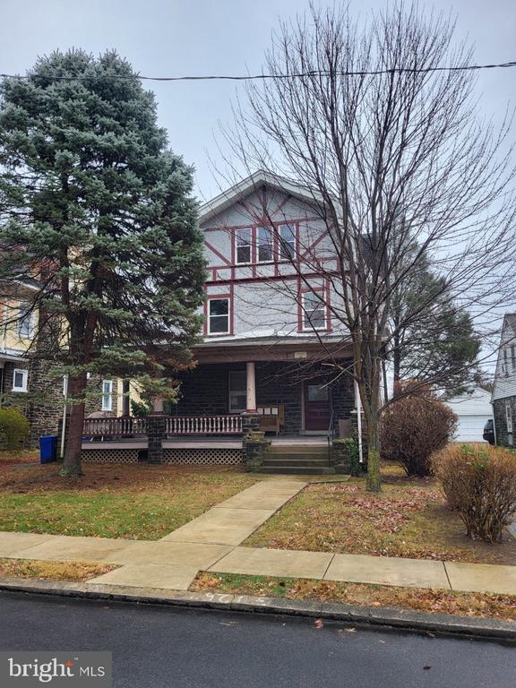 Two-story house with red trim and a covered porch, framed by an evergreen and leafless trees.