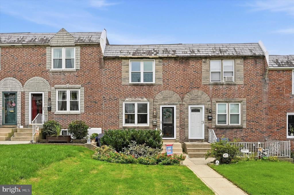 Brick townhouse with stone-arched entryway, front lawn, shrubs, and a walkway.