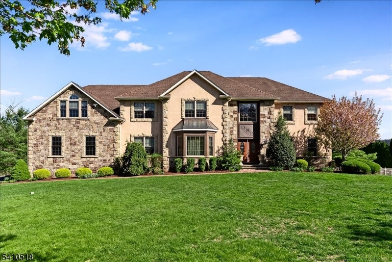 Two-story stone-and-stucco home with a broad green lawn and landscaped shrubs.