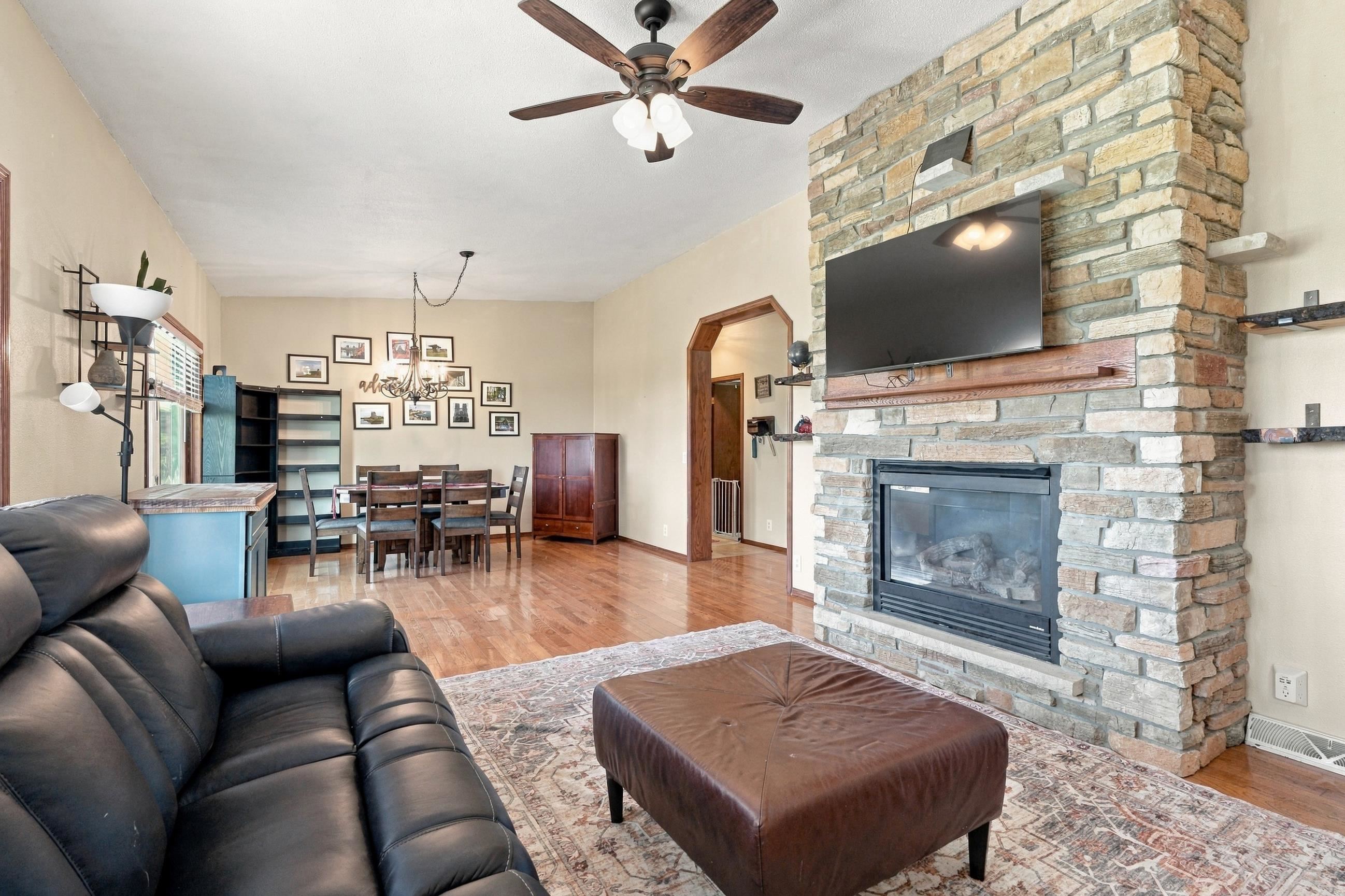 Living room with a floor-to-ceiling stone fireplace, mounted television, leather sofa, and dining area.