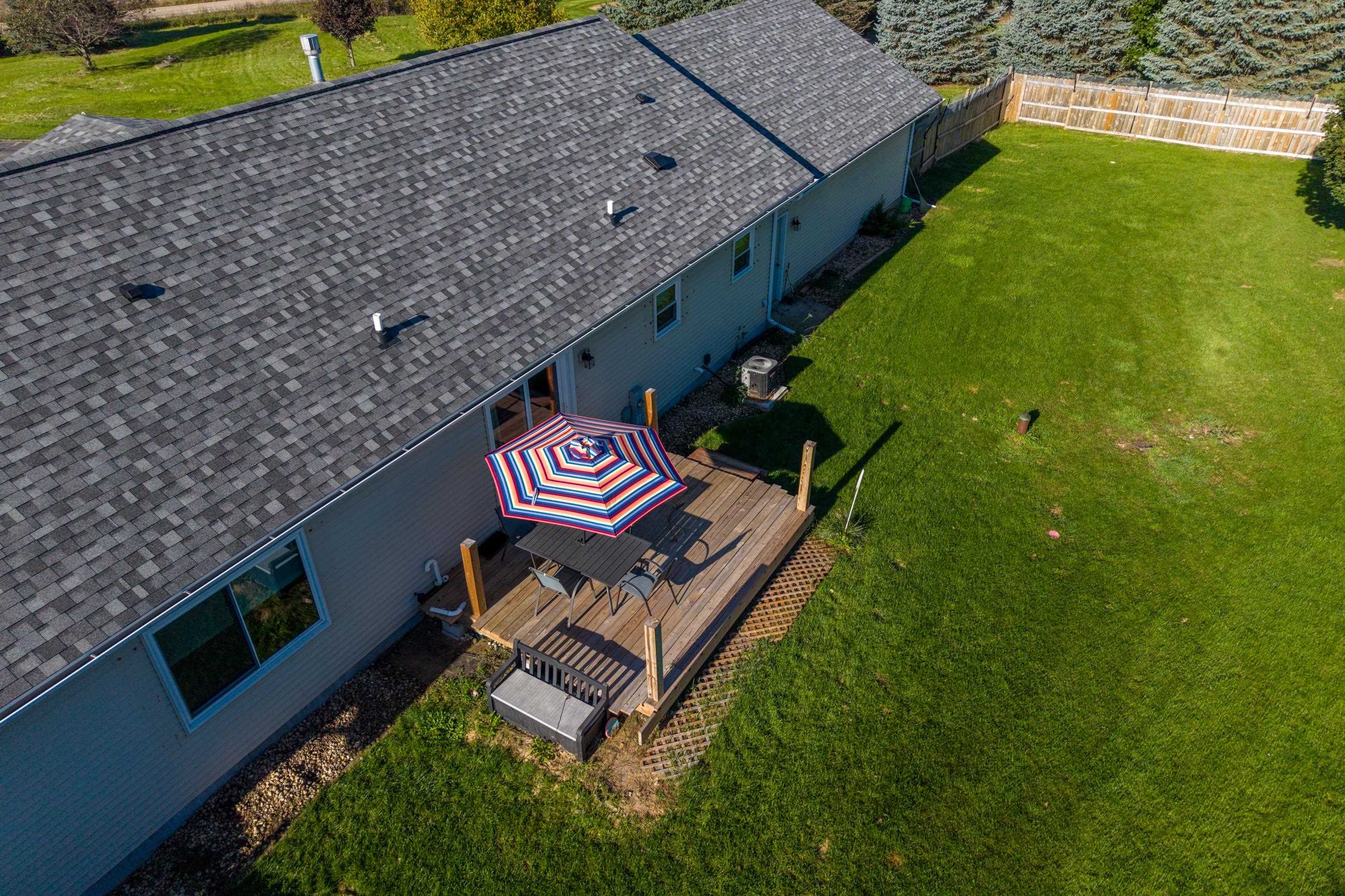 Aerial view of the home’s backyard deck with a striped umbrella, patio table, and broad lawn.
