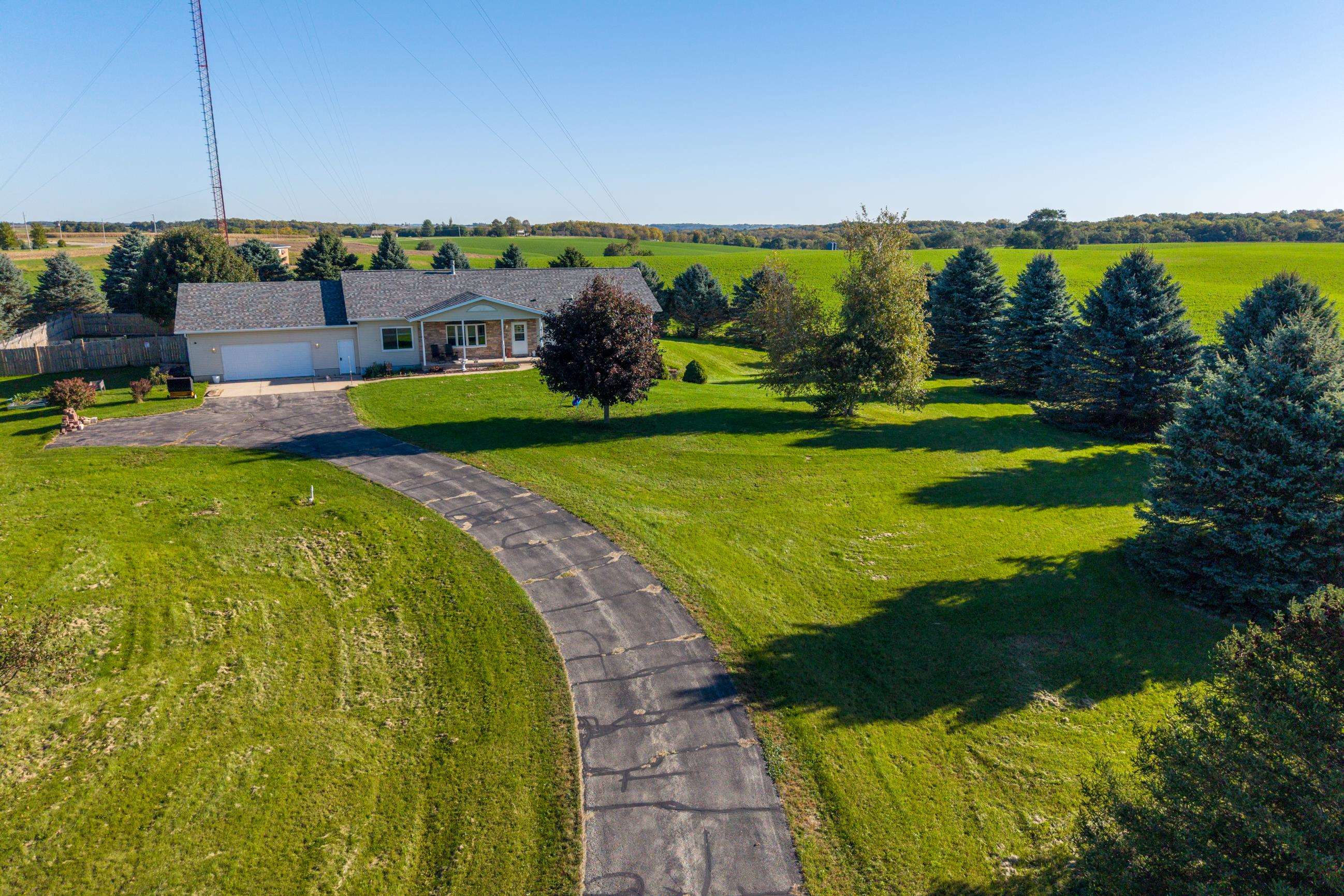 Aerial view of a ranch home with a curved driveway, broad lawn, and surrounding farmland.