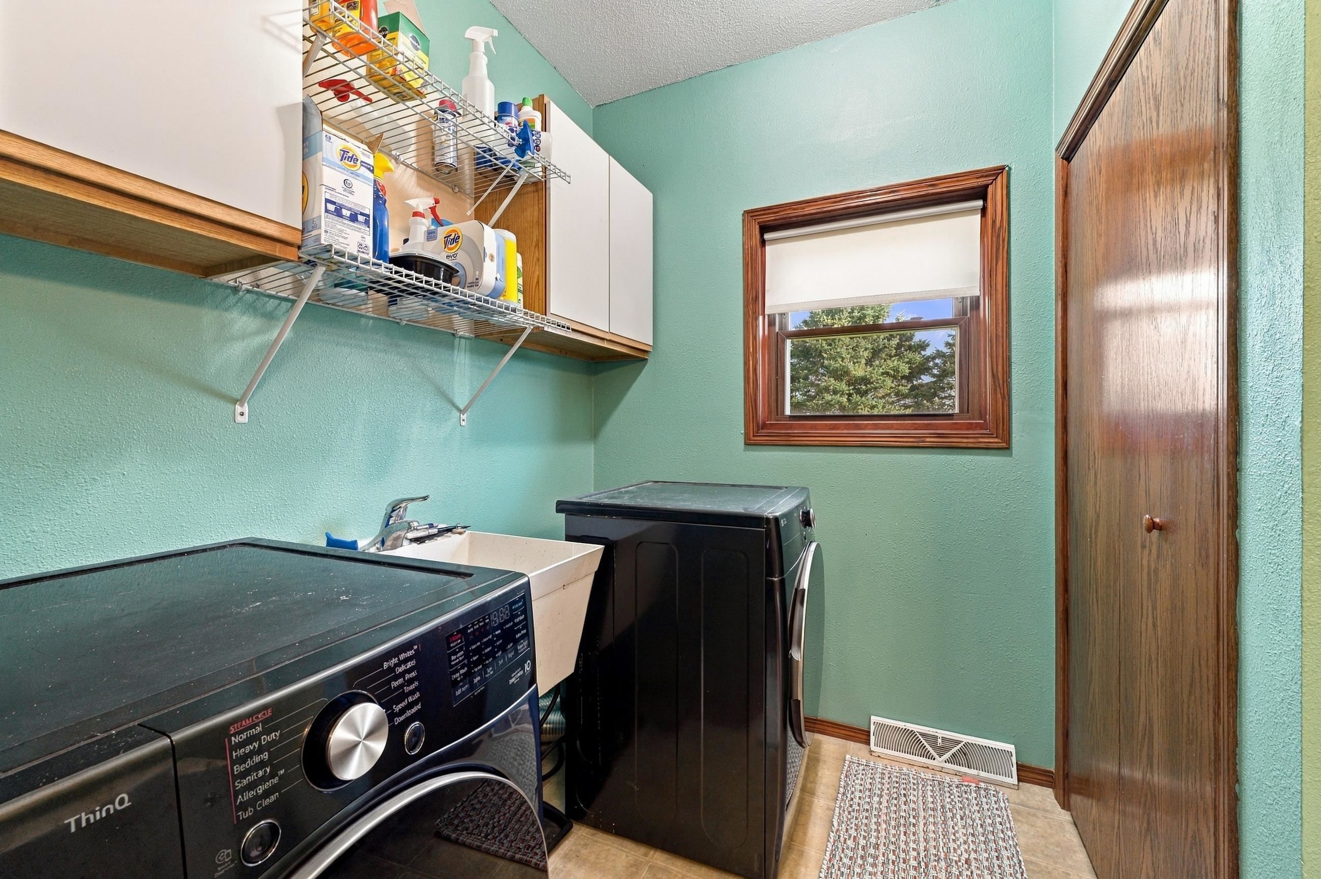 Laundry room with black washer and dryer, utility sink, and overhead storage shelves.