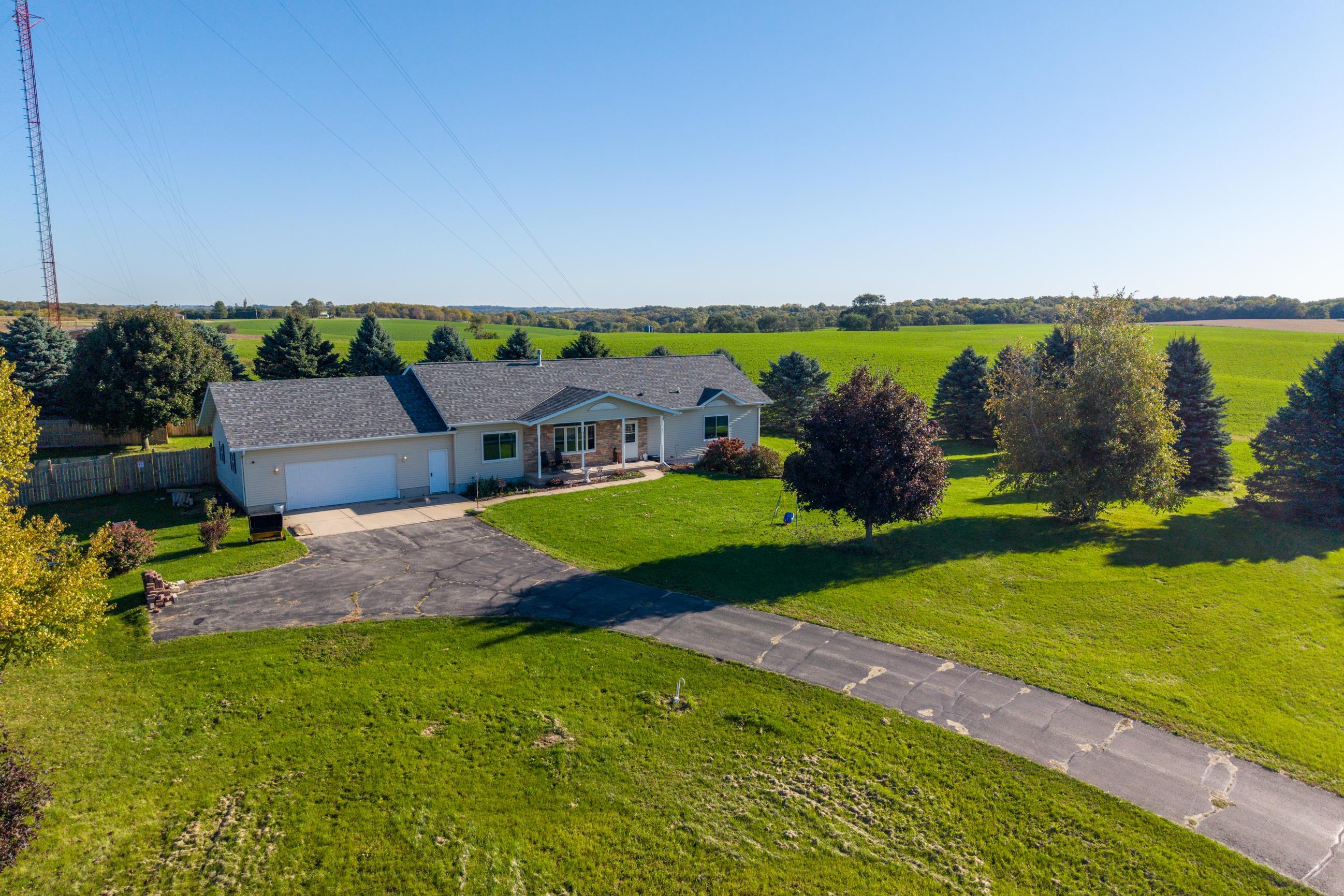 Aerial view of a single-story home, paved driveway, broad lawn, and surrounding farmland.