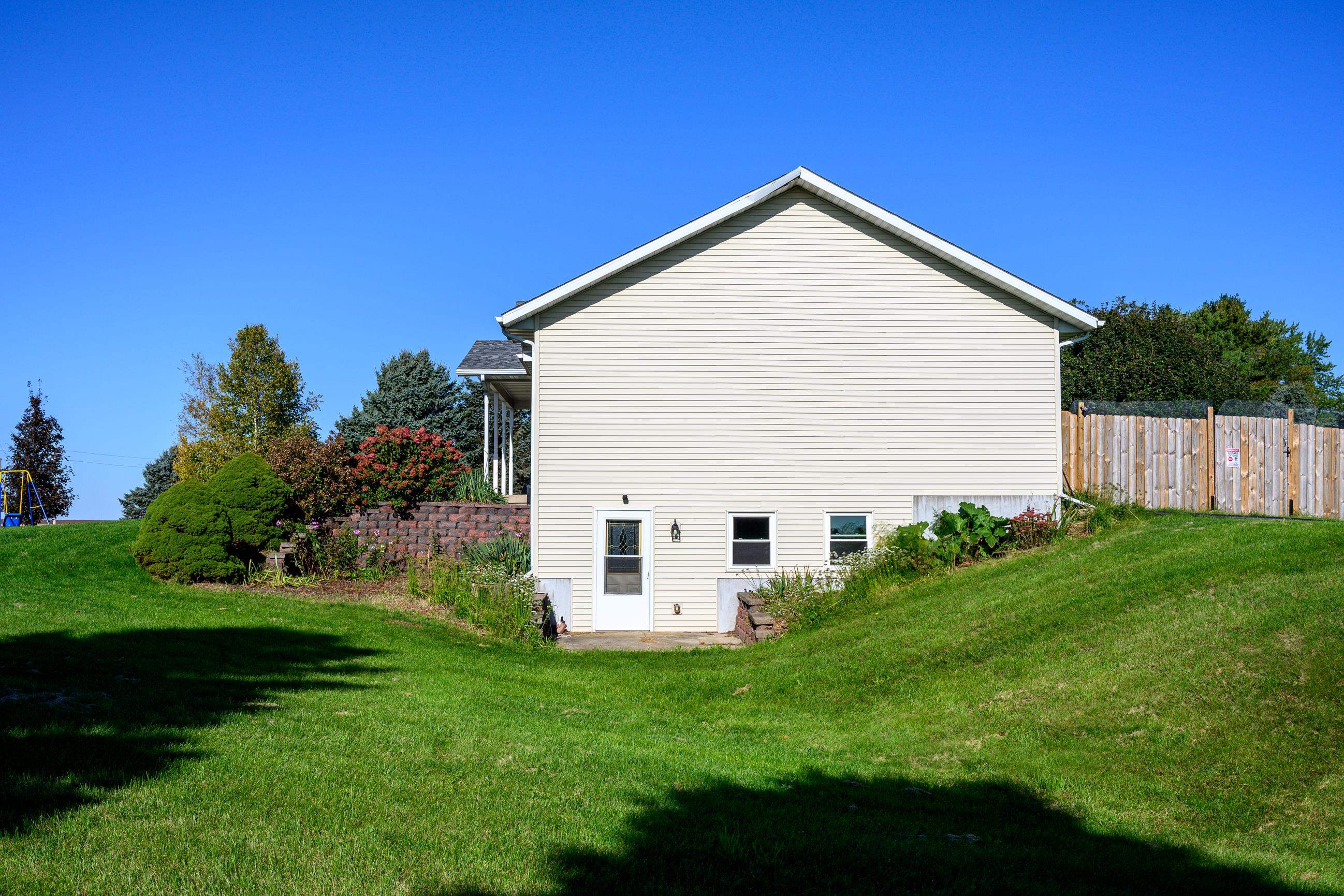 Light-sided house with basement-level door, landscaped retaining wall, and sloping lawn.