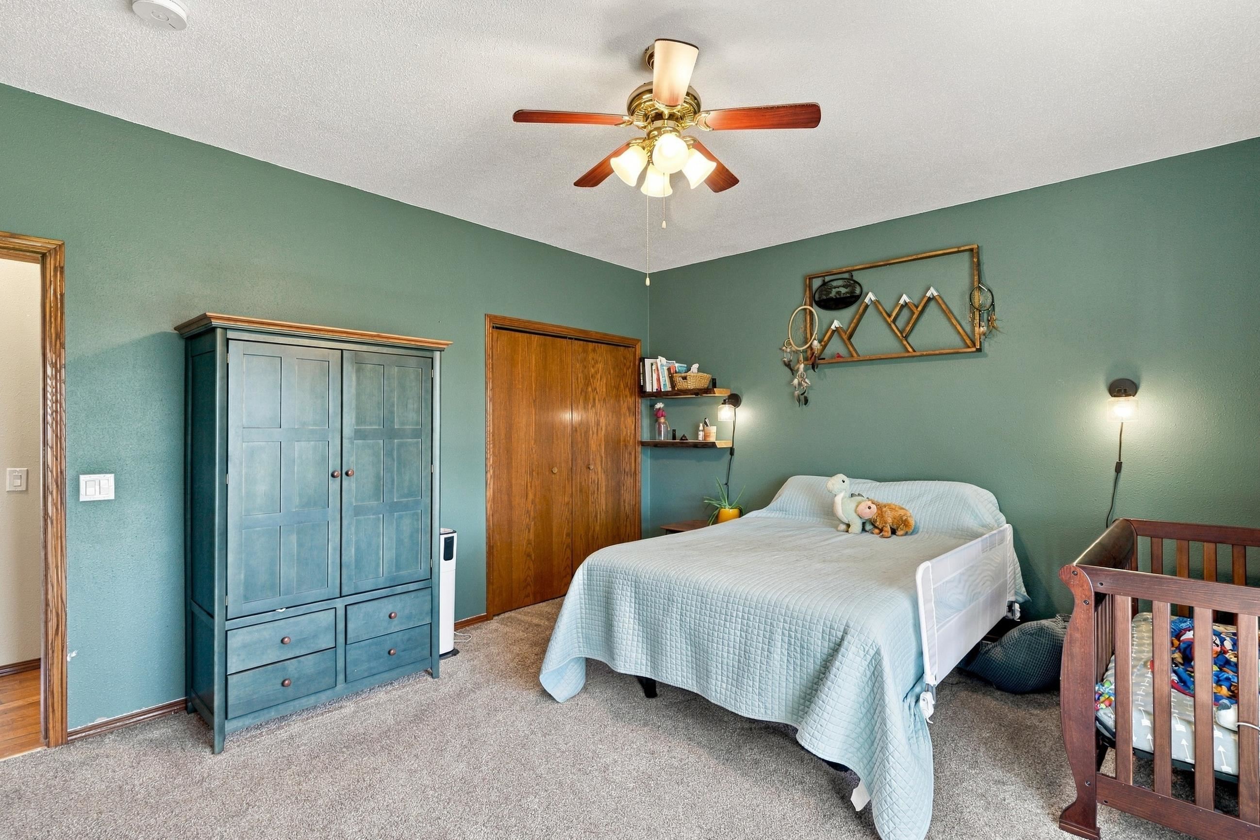 Bedroom with a teal wardrobe, light blue bedspread, and wooden crib.