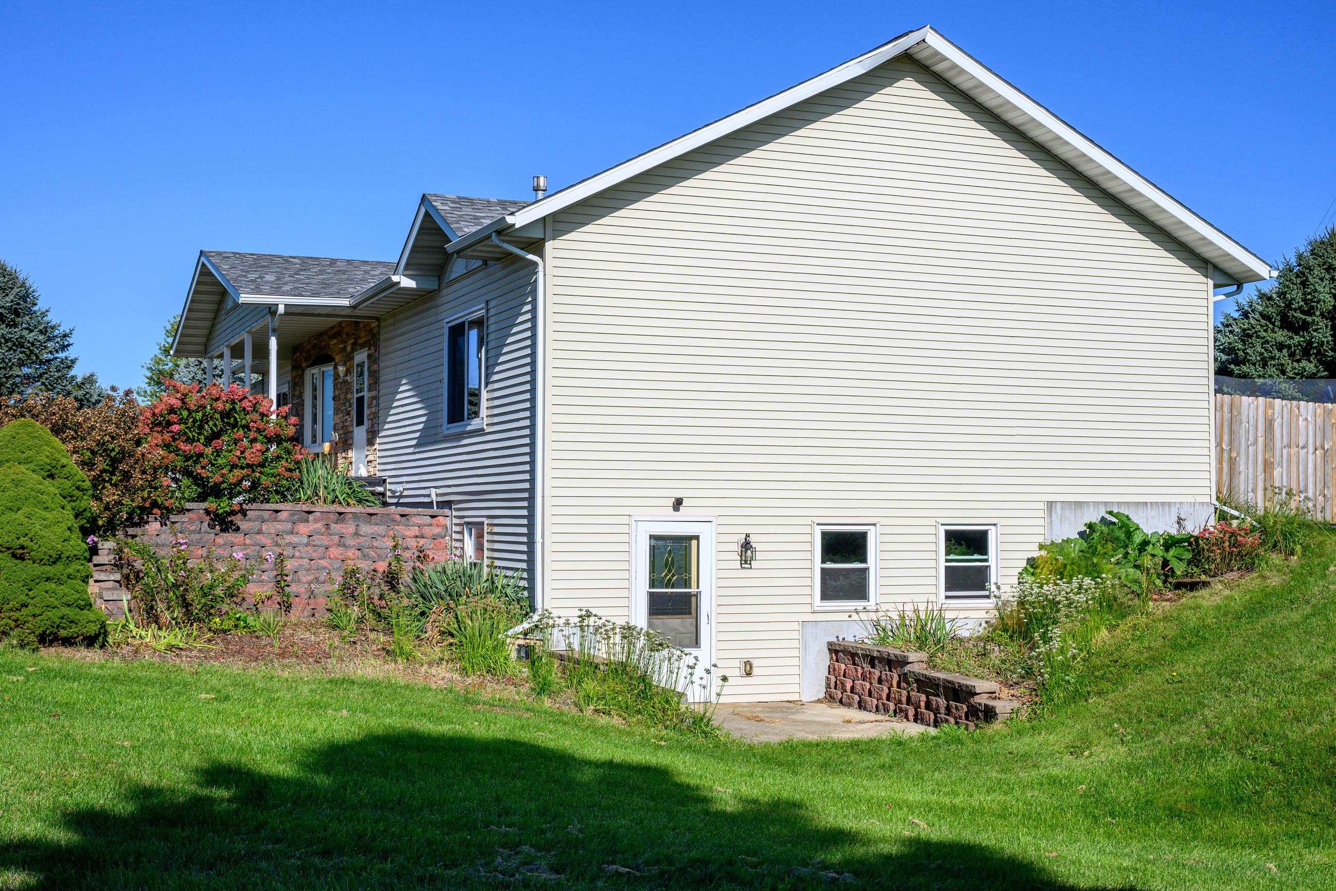 House side exterior with light siding, lower-level door, landscaped retaining walls, and lawn.
