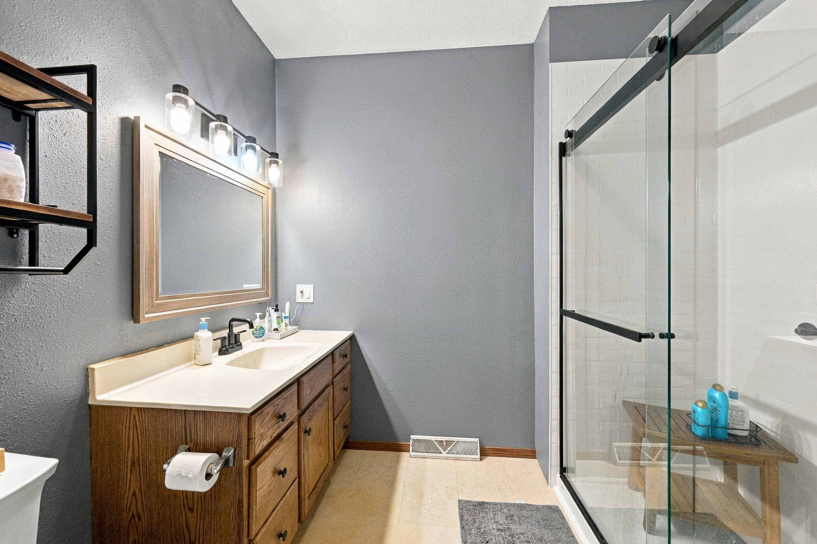 Bathroom with a wood vanity and a glass-enclosed tiled shower.