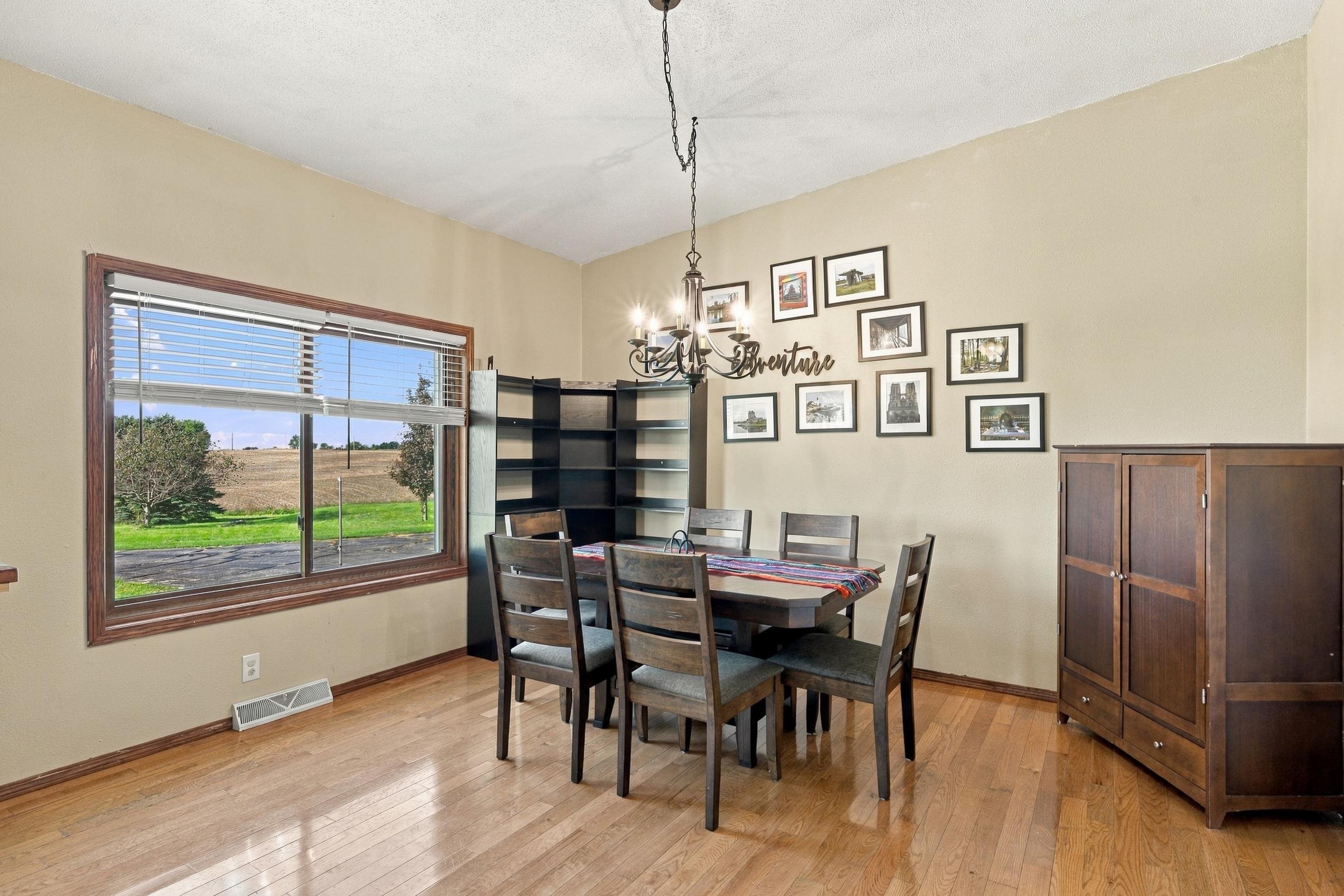 Dining room with a wood table, framed wall art, and a large window overlooking open fields.