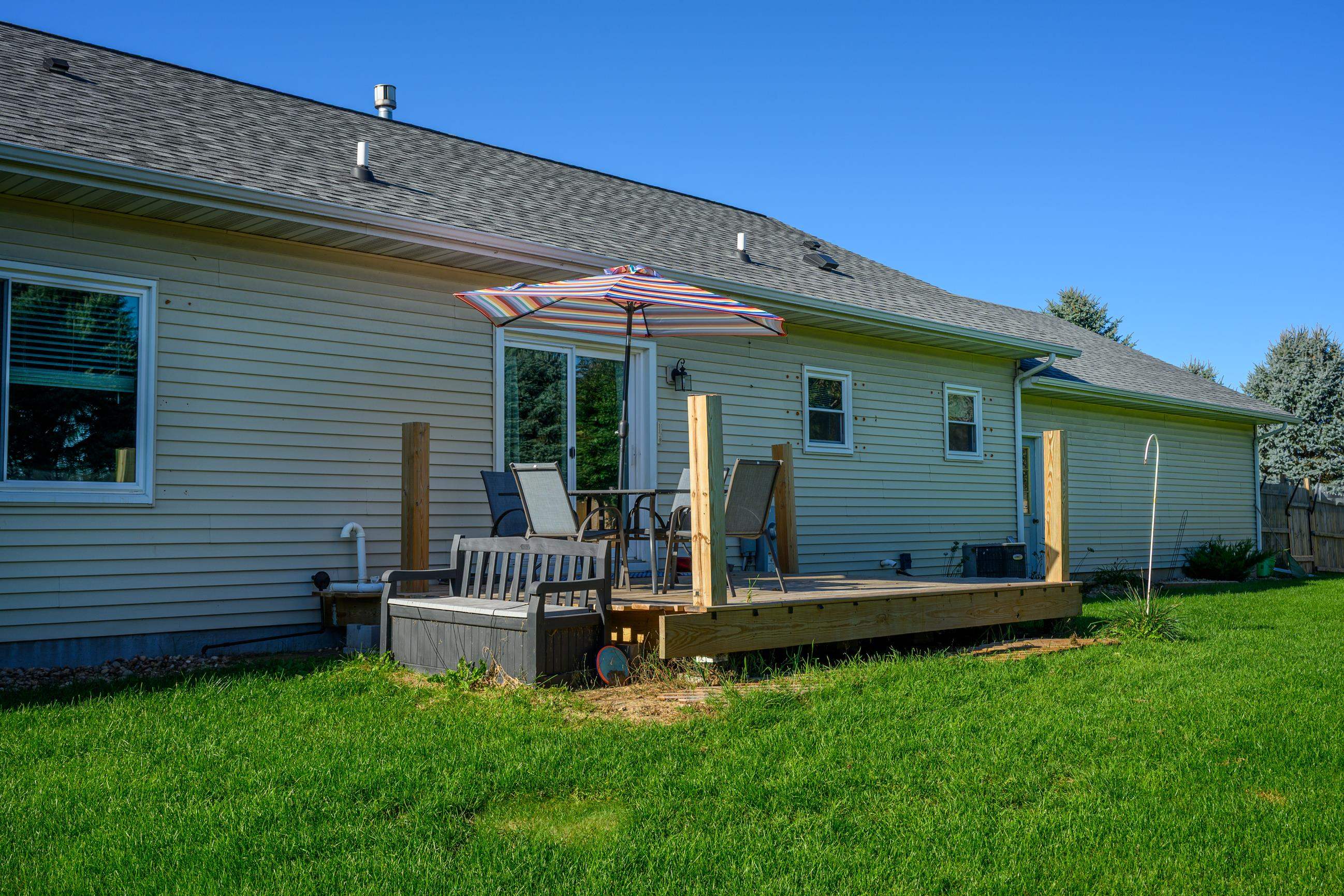 Rear of a house with a raised deck, patio furniture, and a striped umbrella.