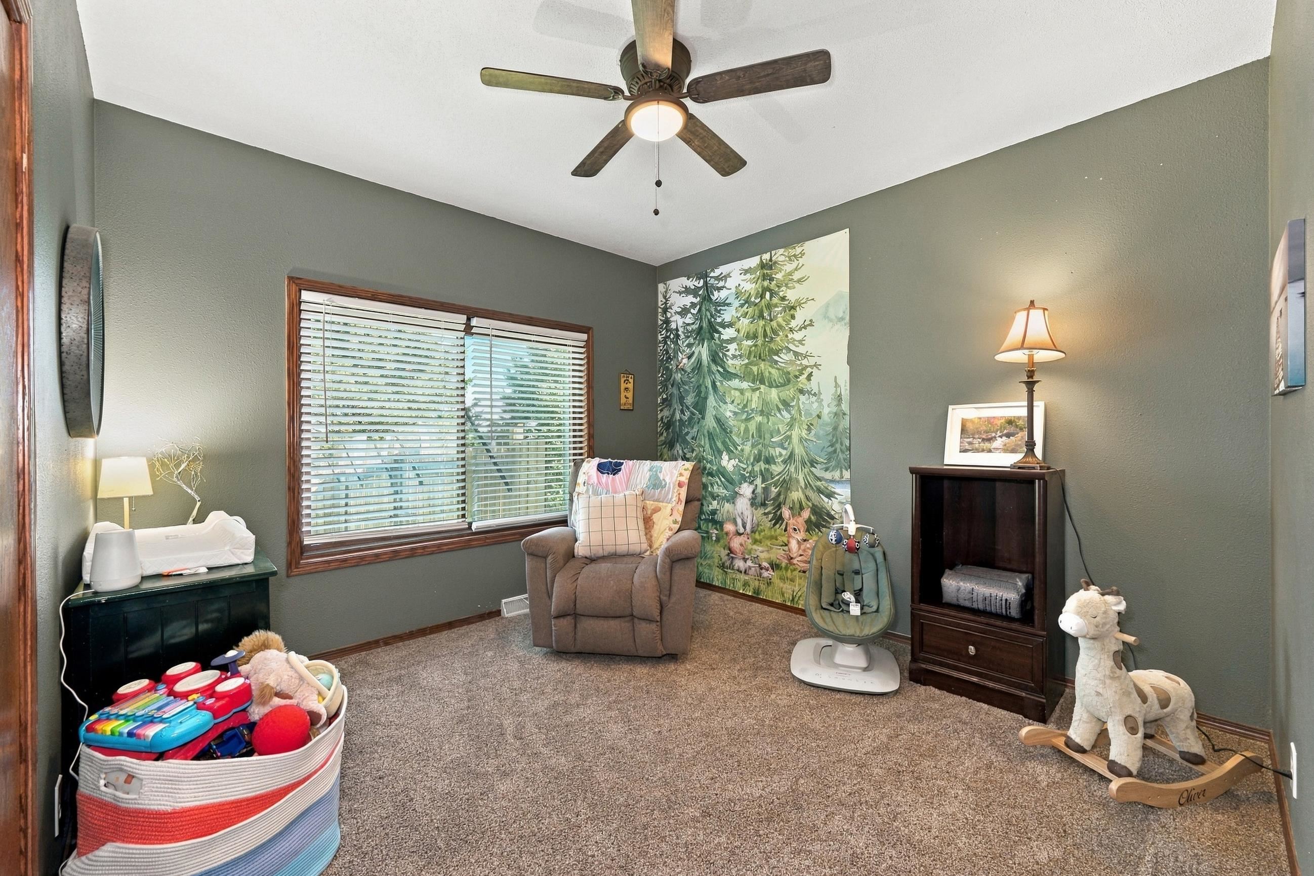 Furnished nursery with a woodland mural, recliner, infant seat, and toys.