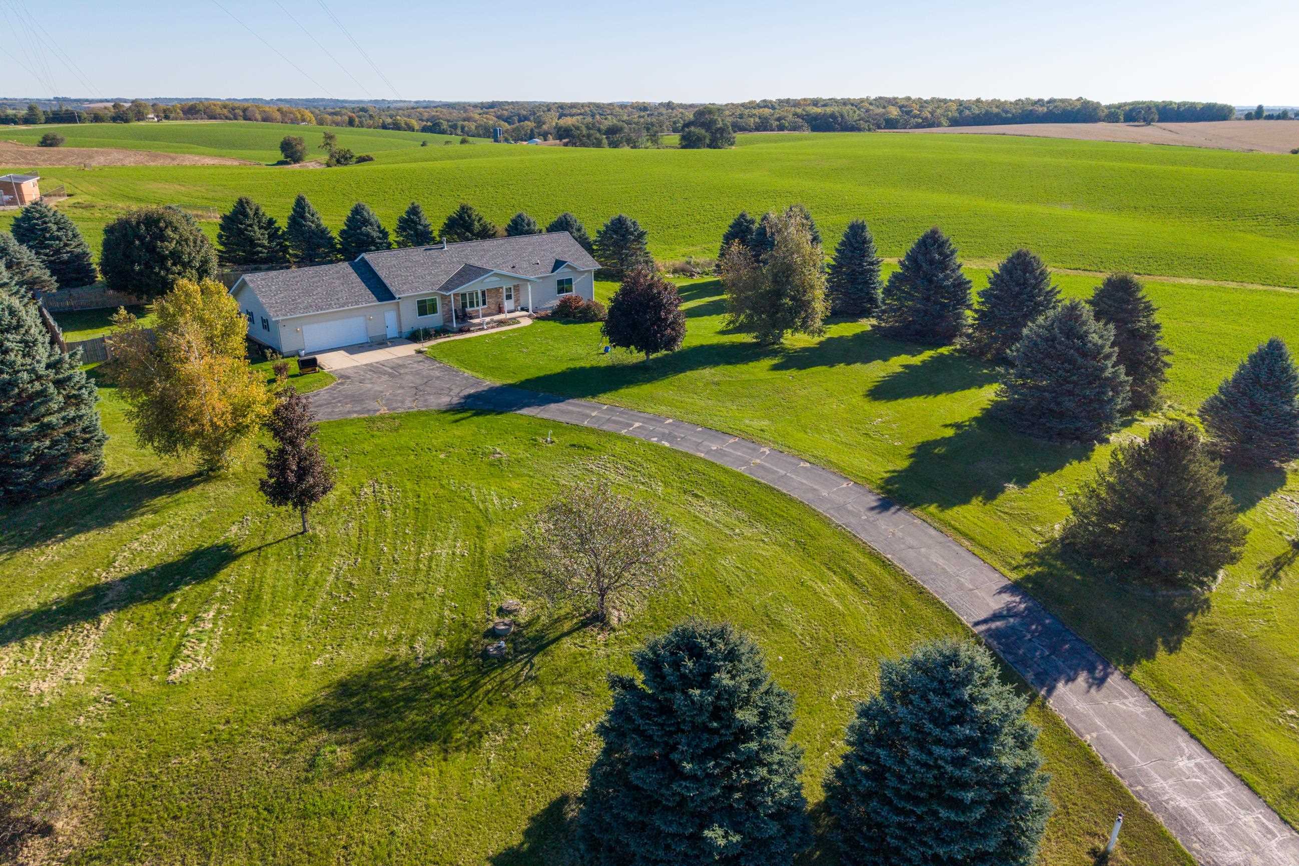 Aerial view of a ranch home surrounded by a broad lawn, mature trees, and green fields.