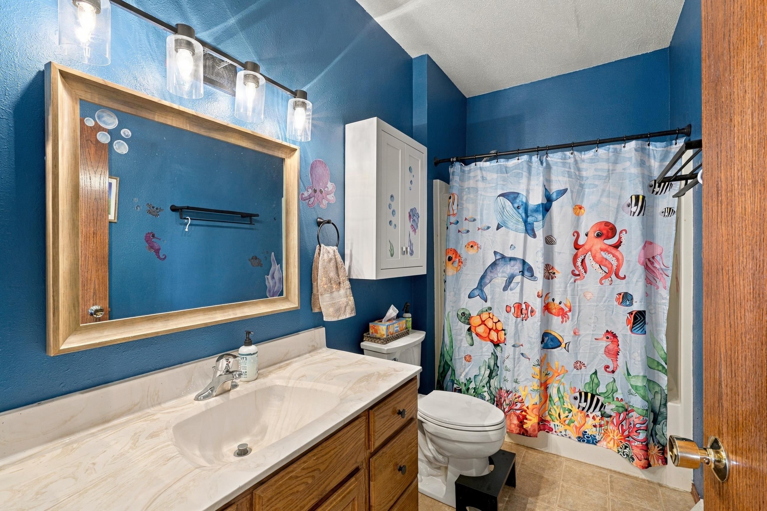 Bathroom with a marble vanity, deep blue walls, and a colorful sea-life shower curtain.
