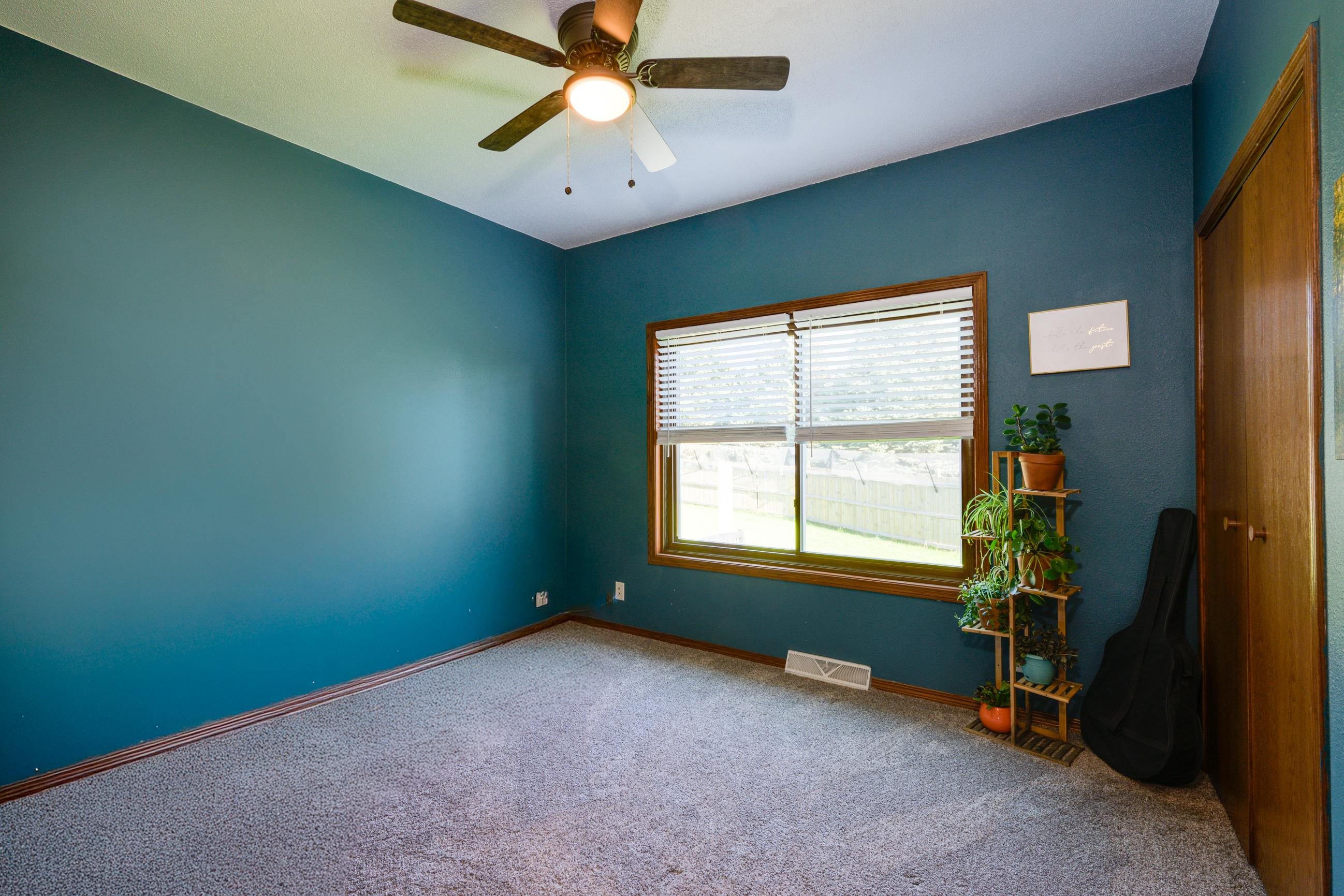 Carpeted bedroom with teal walls, a wide window, ceiling fan, and wooden closet doors.