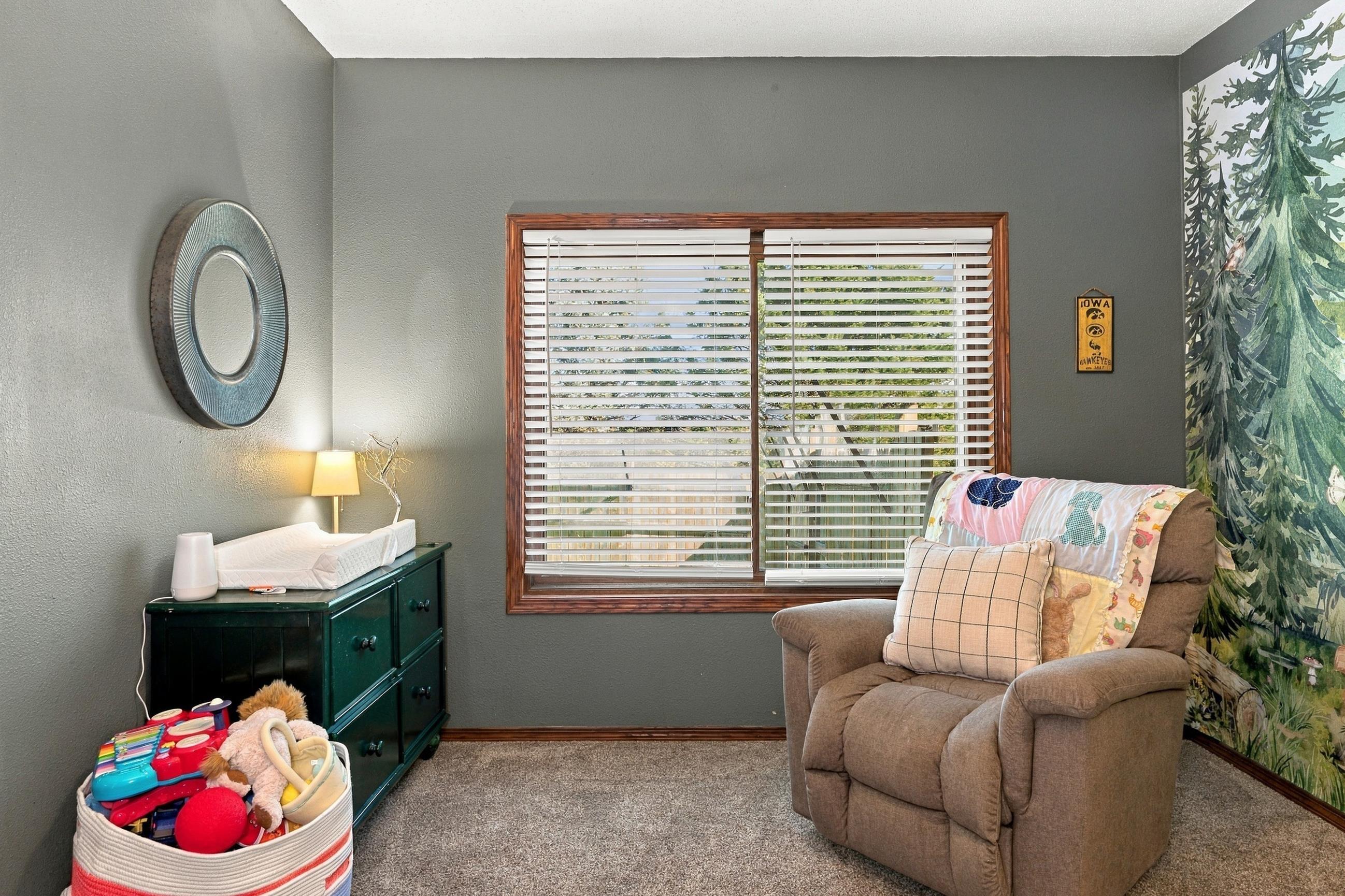 Furnished nursery with a recliner, toy basket, changing table, and woodland mural.