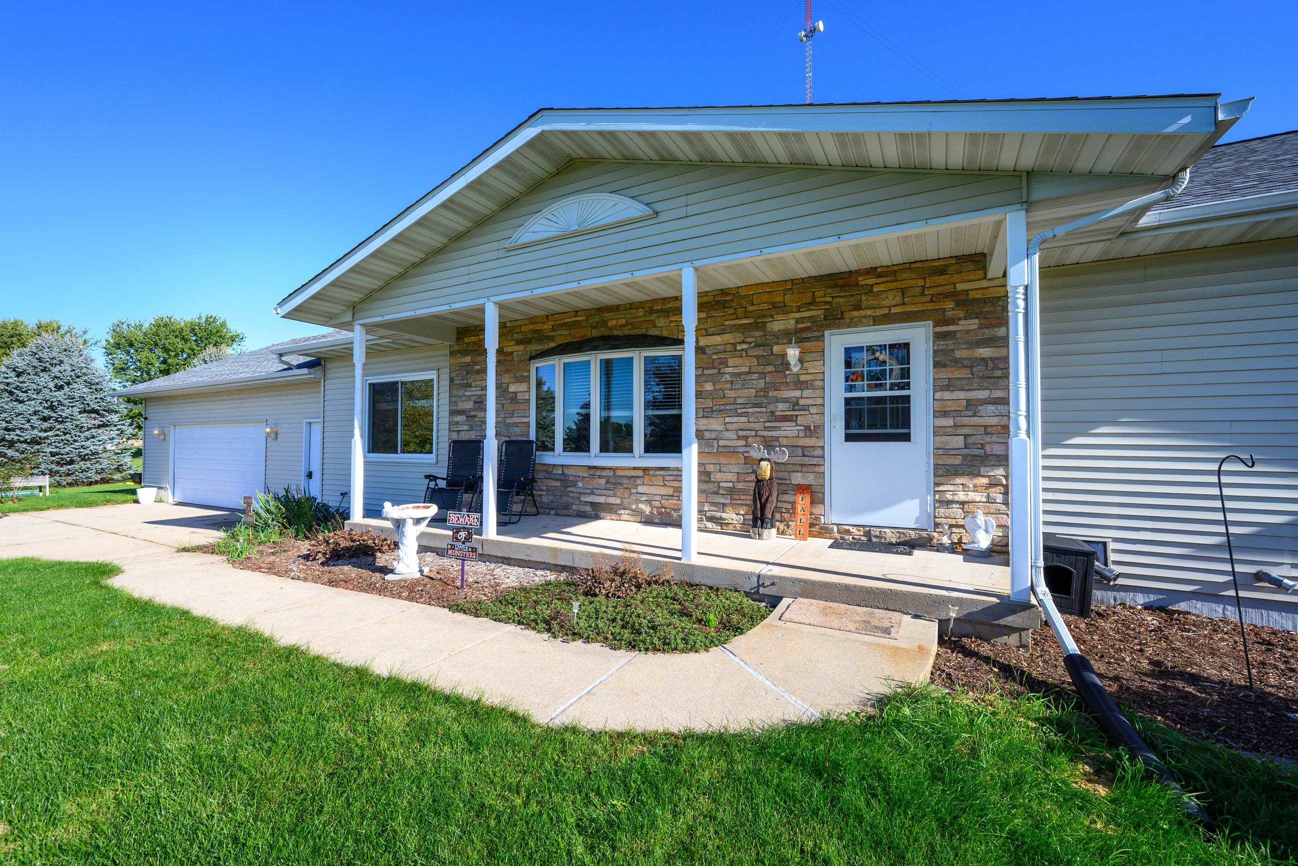 House with a stone-fronted covered porch, attached garage, and green lawn.