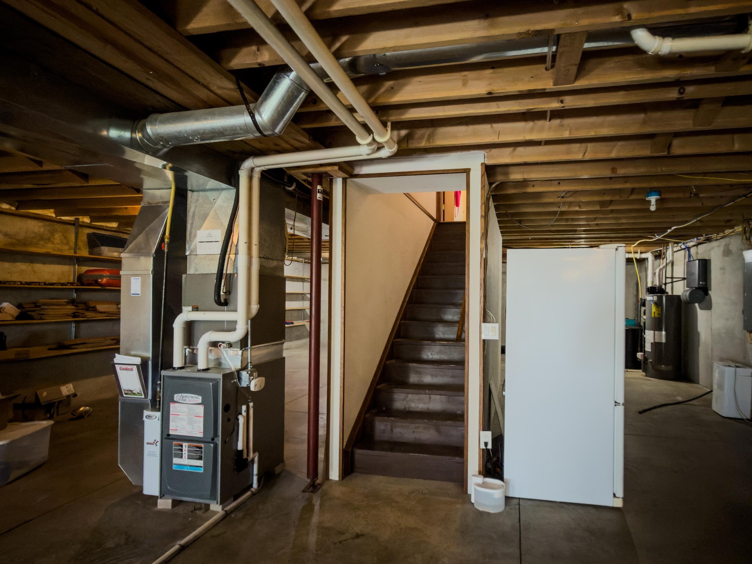 Unfinished basement with exposed joists, furnace, water heater, and stairs.