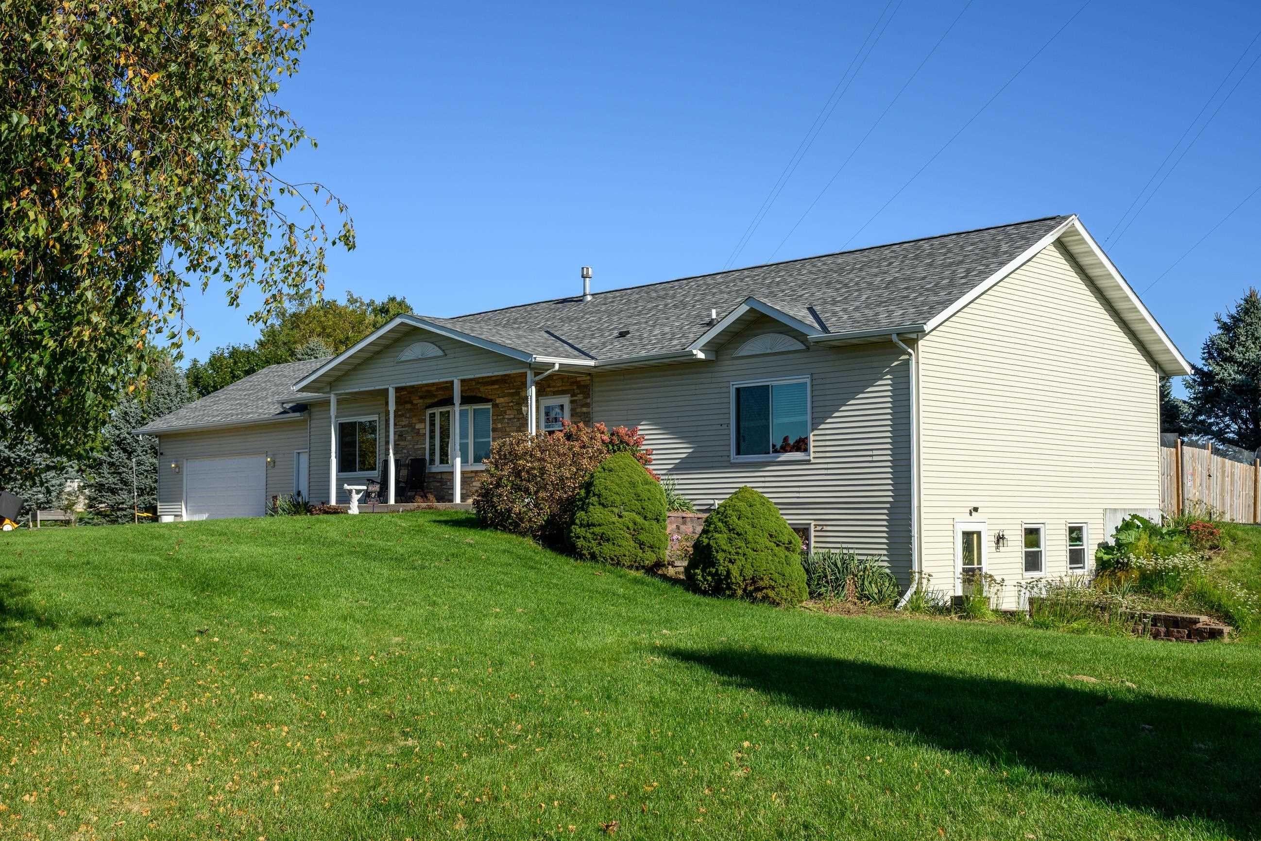 House exterior with a covered entry, stone facade, attached garage, and landscaped lawn.