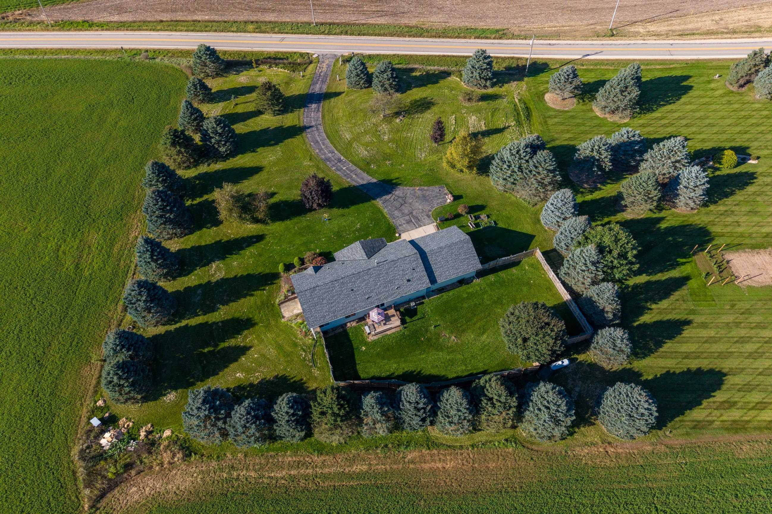 Aerial view of a home with a curved driveway, landscaped lawn, and tree-lined grounds.