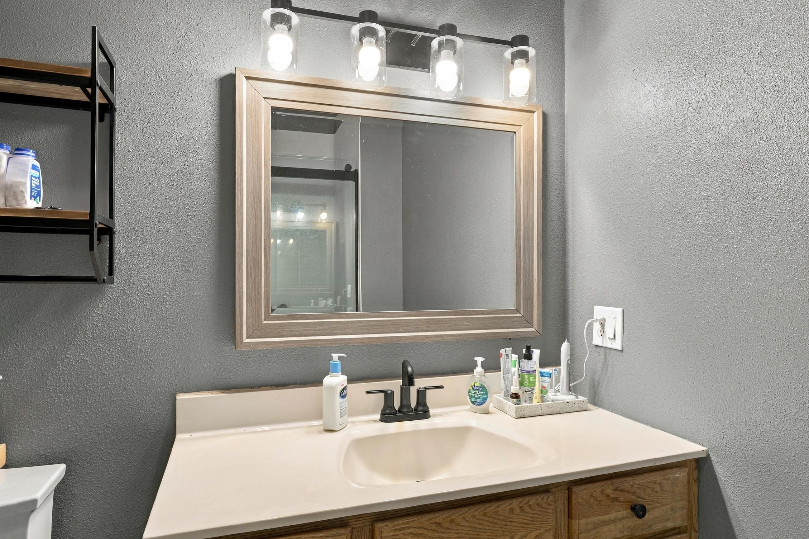 Bathroom vanity with a cream sink, wood-framed mirror, and bright four-bulb light fixture.