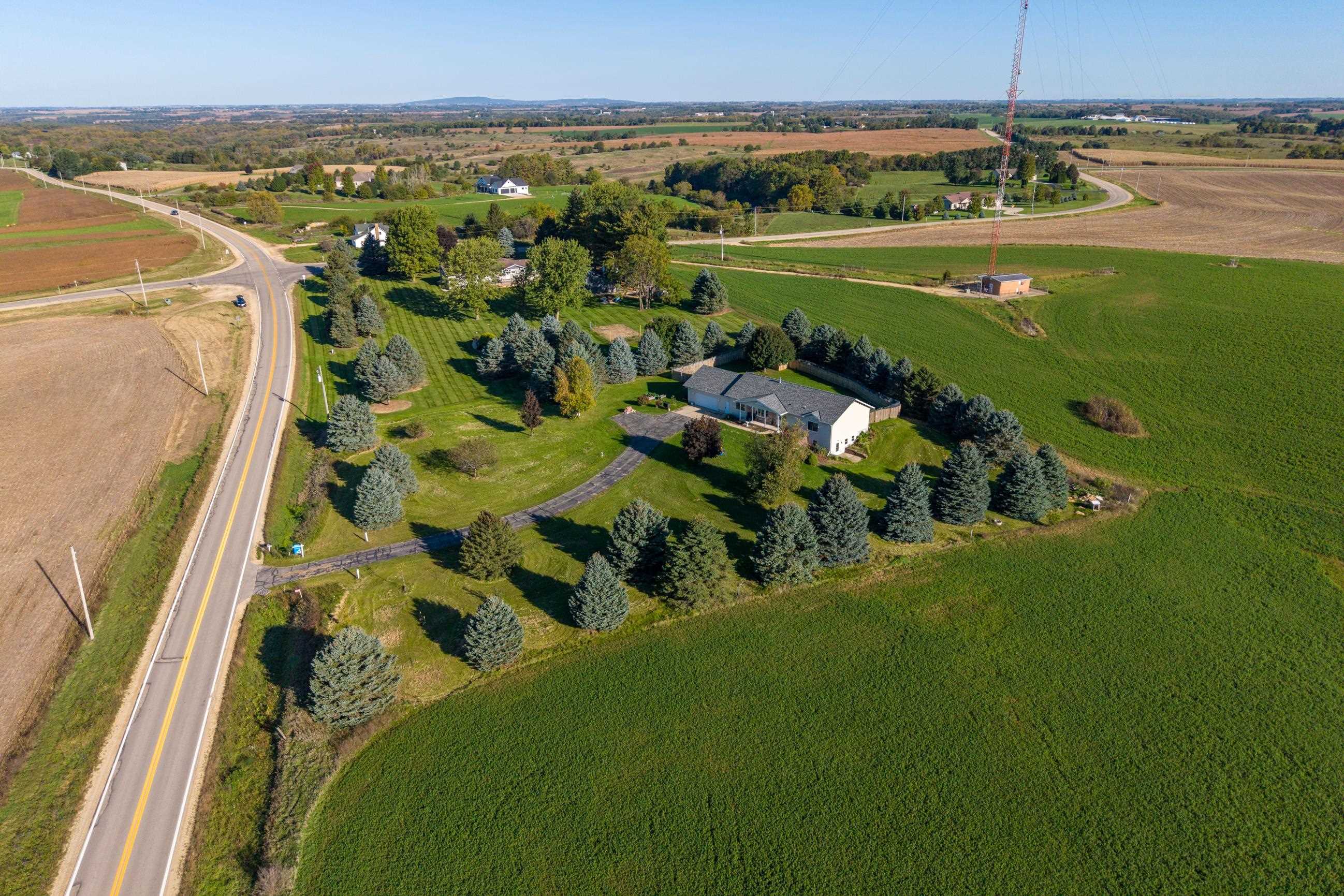 Aerial view of a white home surrounded by evergreen trees, farmland, and a two-lane road.