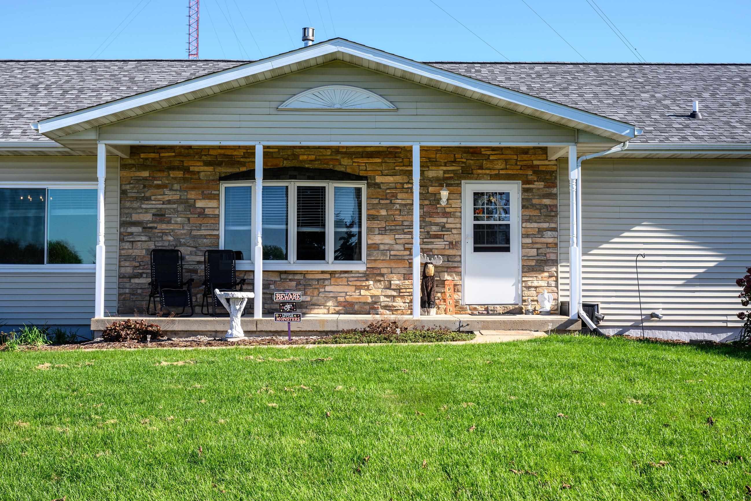 Home with a stone-front covered porch, white entry door, and two black chairs.