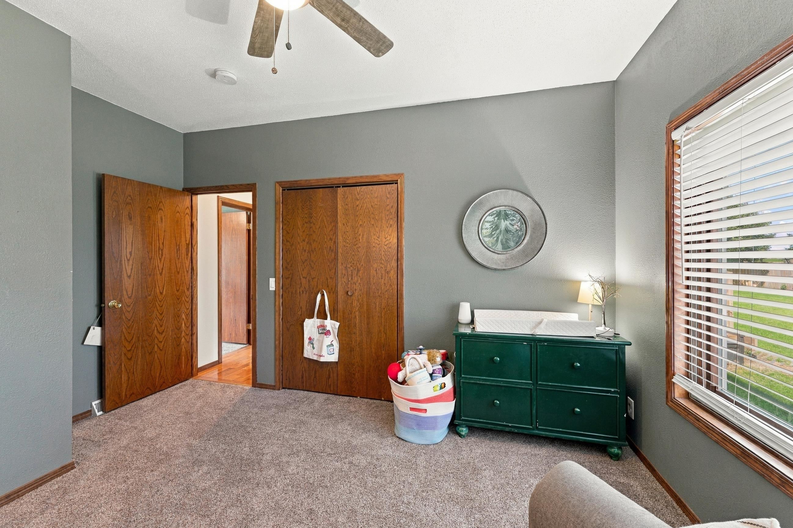 Bedroom with gray walls, wood trim, a green dresser, and a large window with blinds.