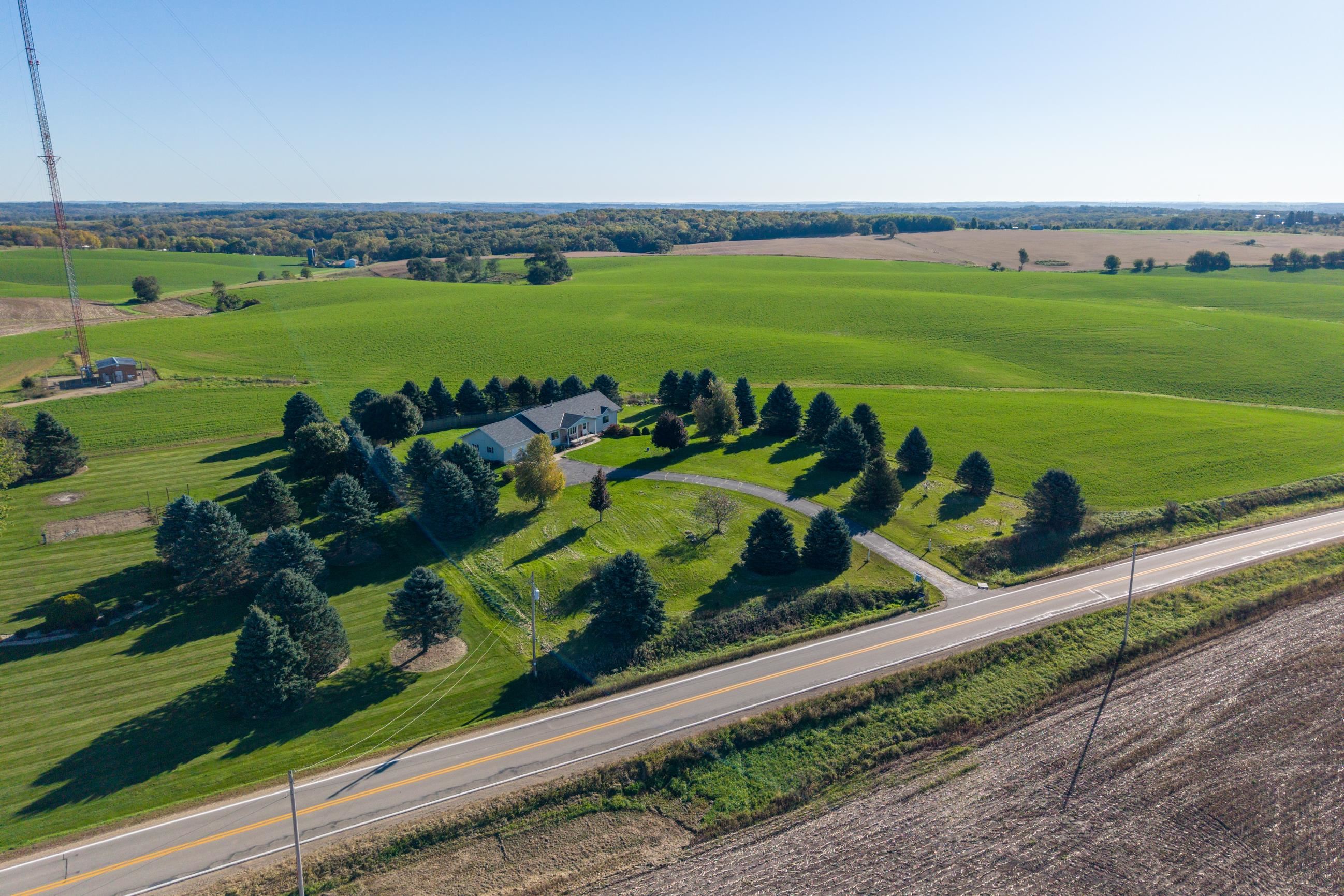 Aerial view of a rural home surrounded by lawns and evergreen trees beside a highway.