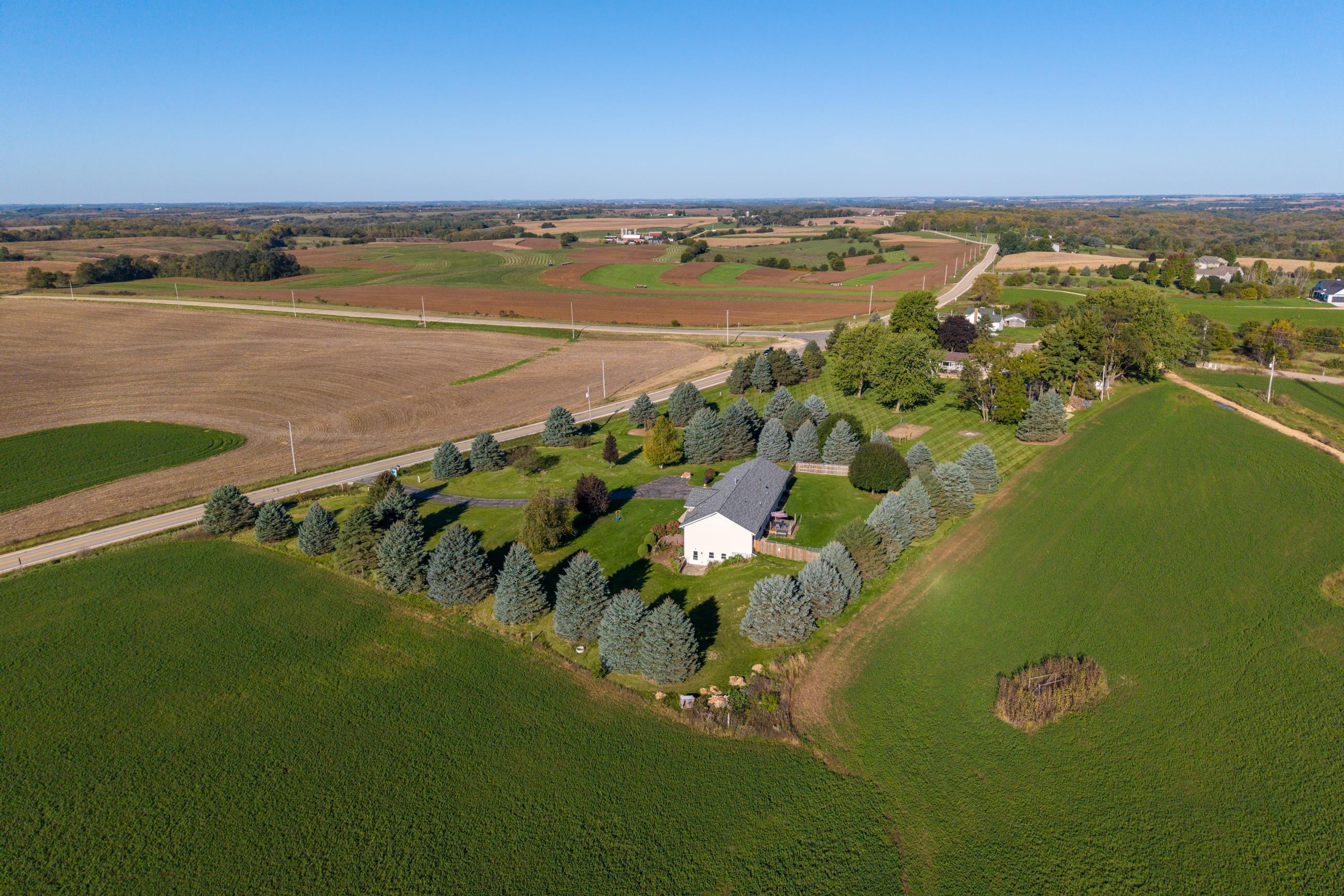 Aerial view of a rural home surrounded by evergreen trees, farmland, and open fields.