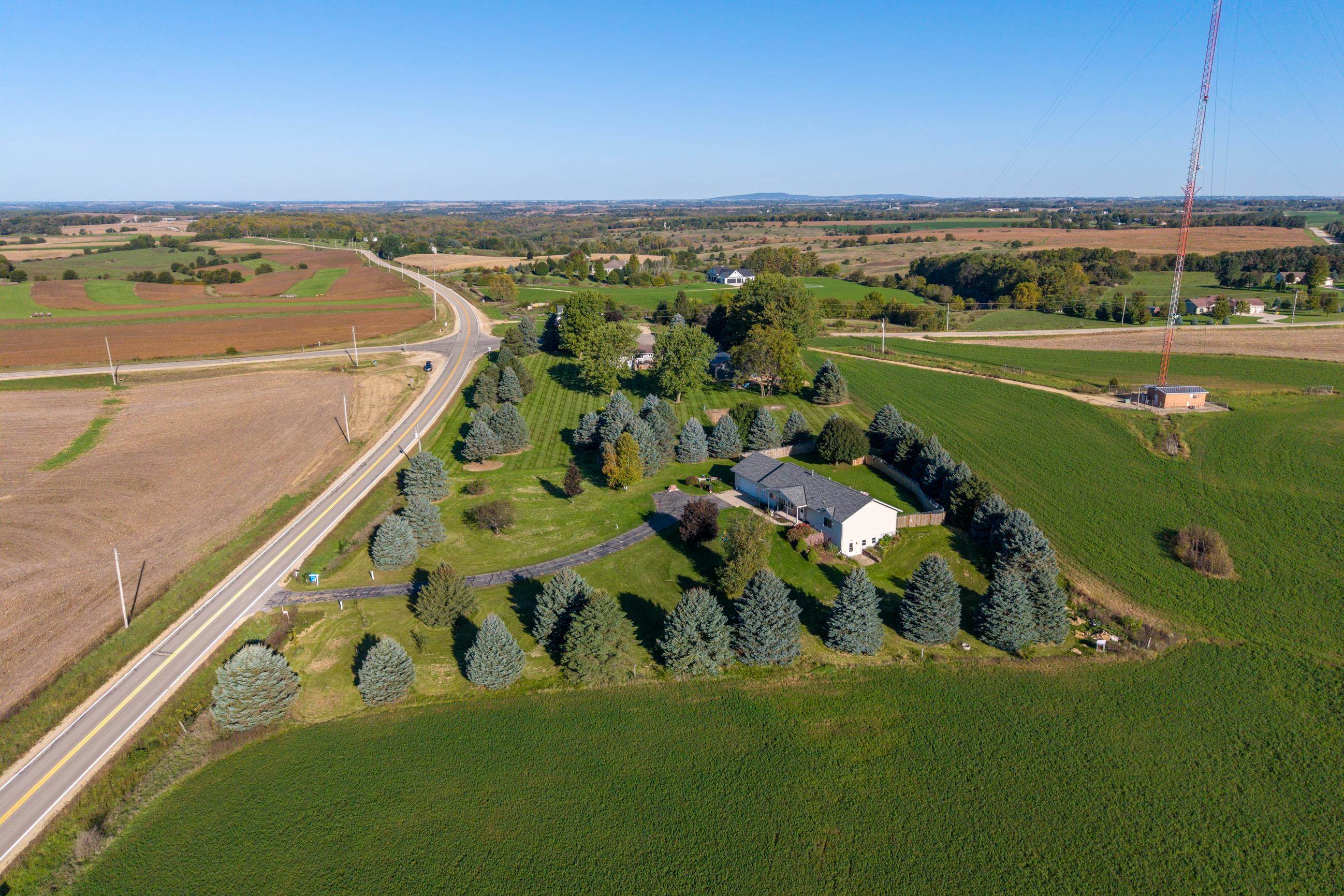 Aerial view of a rural home surrounded by evergreen trees, fields, and a highway.