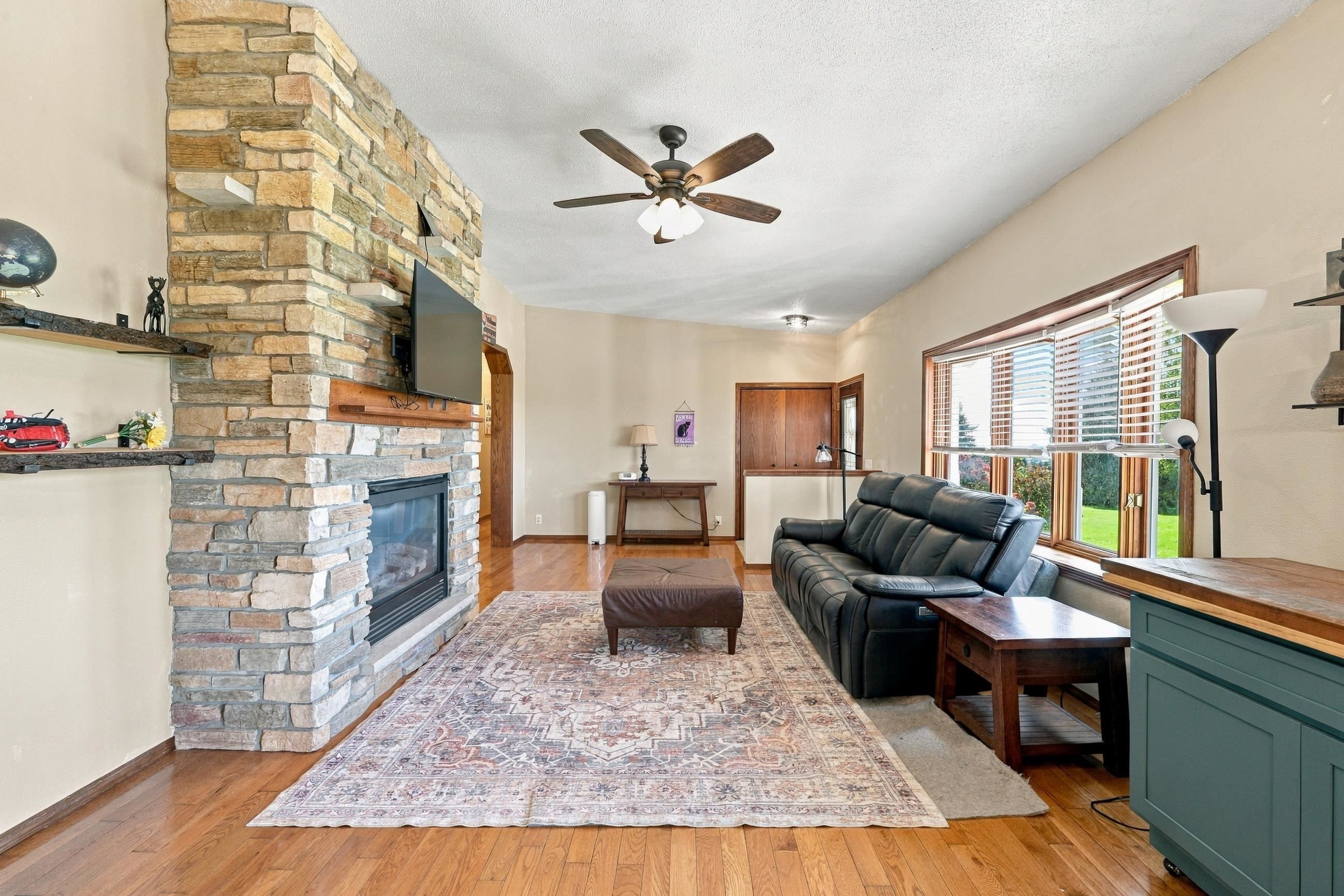 Living room with a stone fireplace, leather sofa, and large windows overlooking the lawn.