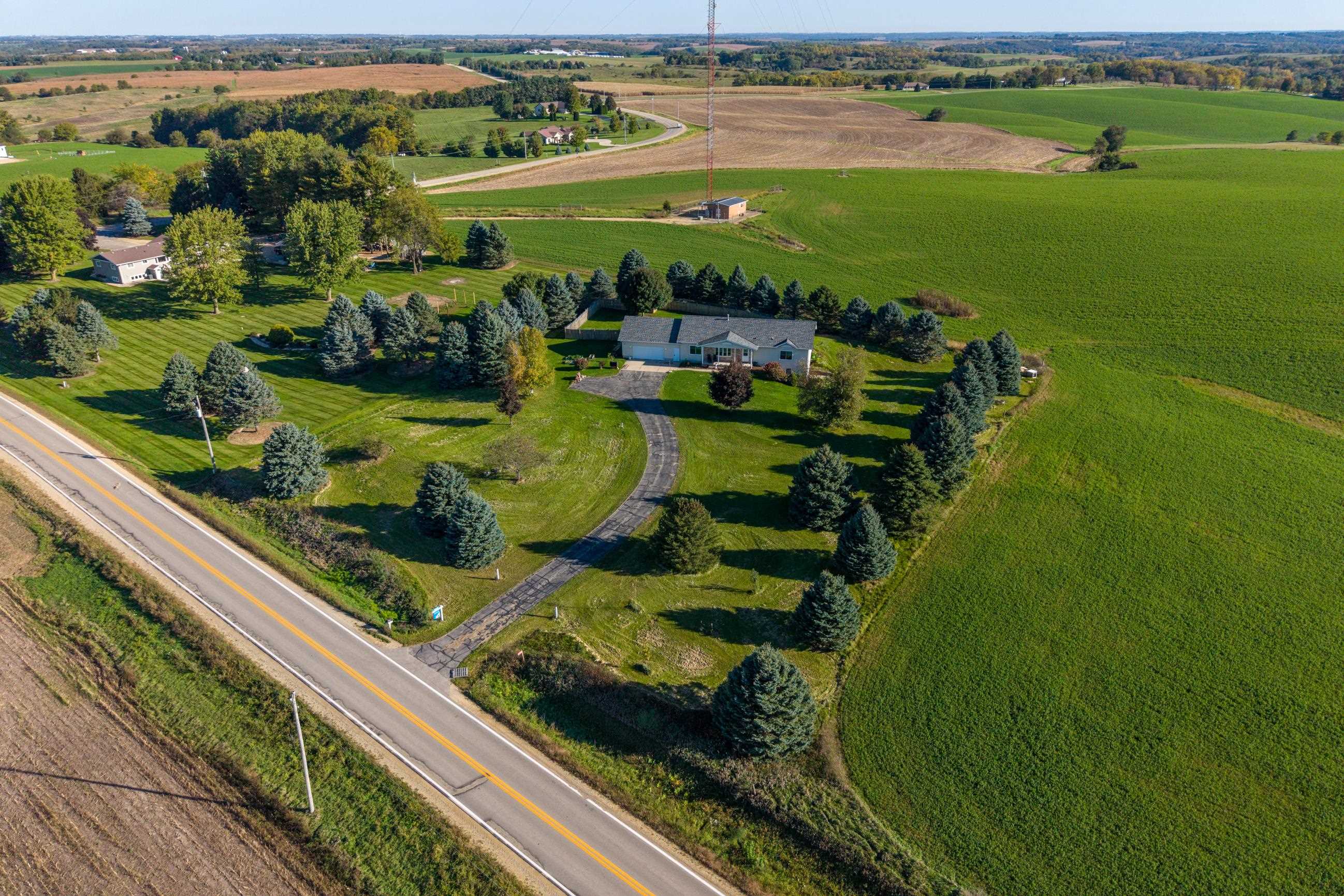 Aerial view of a rural home with a curved driveway, mature trees, and surrounding farmland.