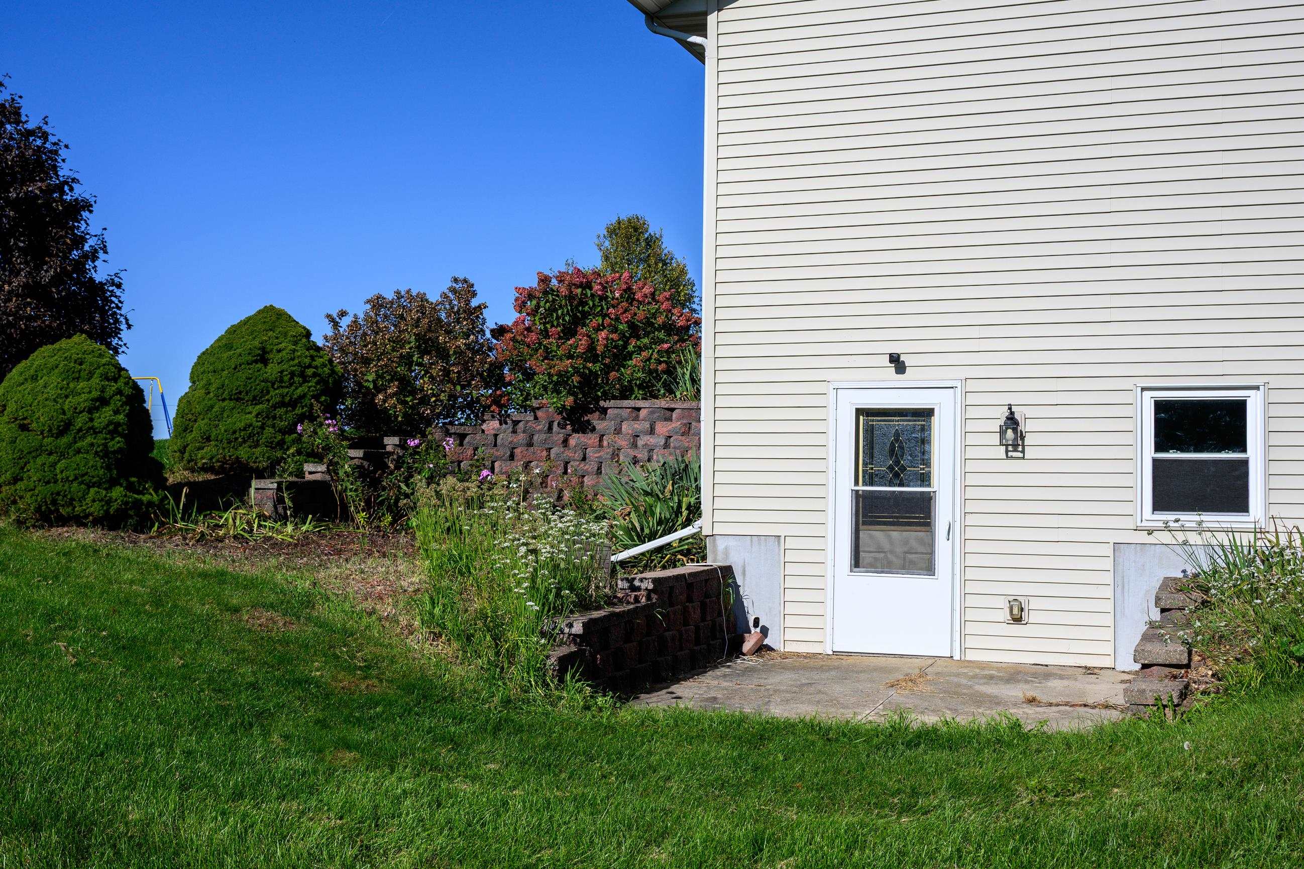 Side entrance with a glass storm door beside landscaped retaining walls and lawn.