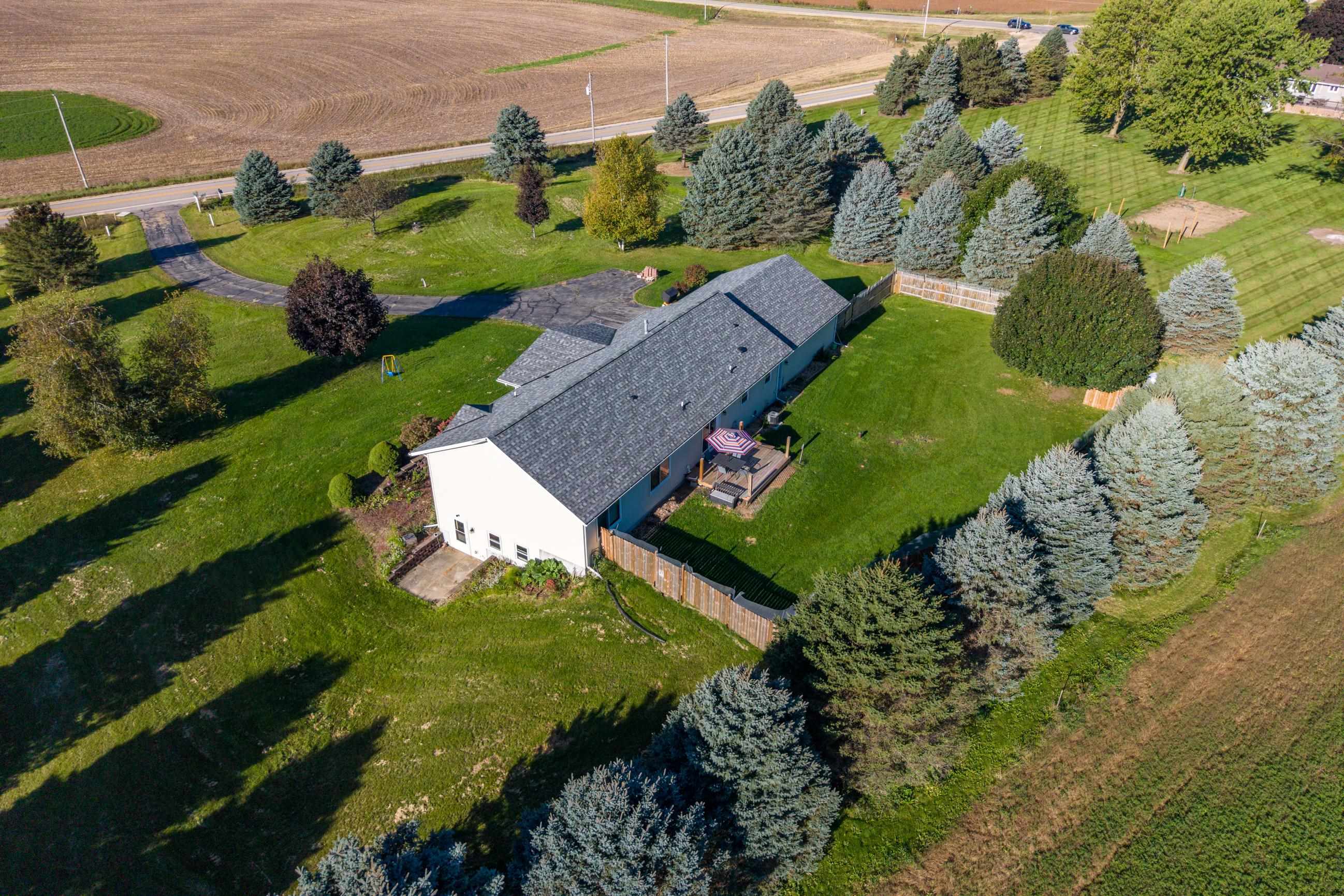 Aerial view of a home with a spacious lawn, mature evergreens, and a deck.