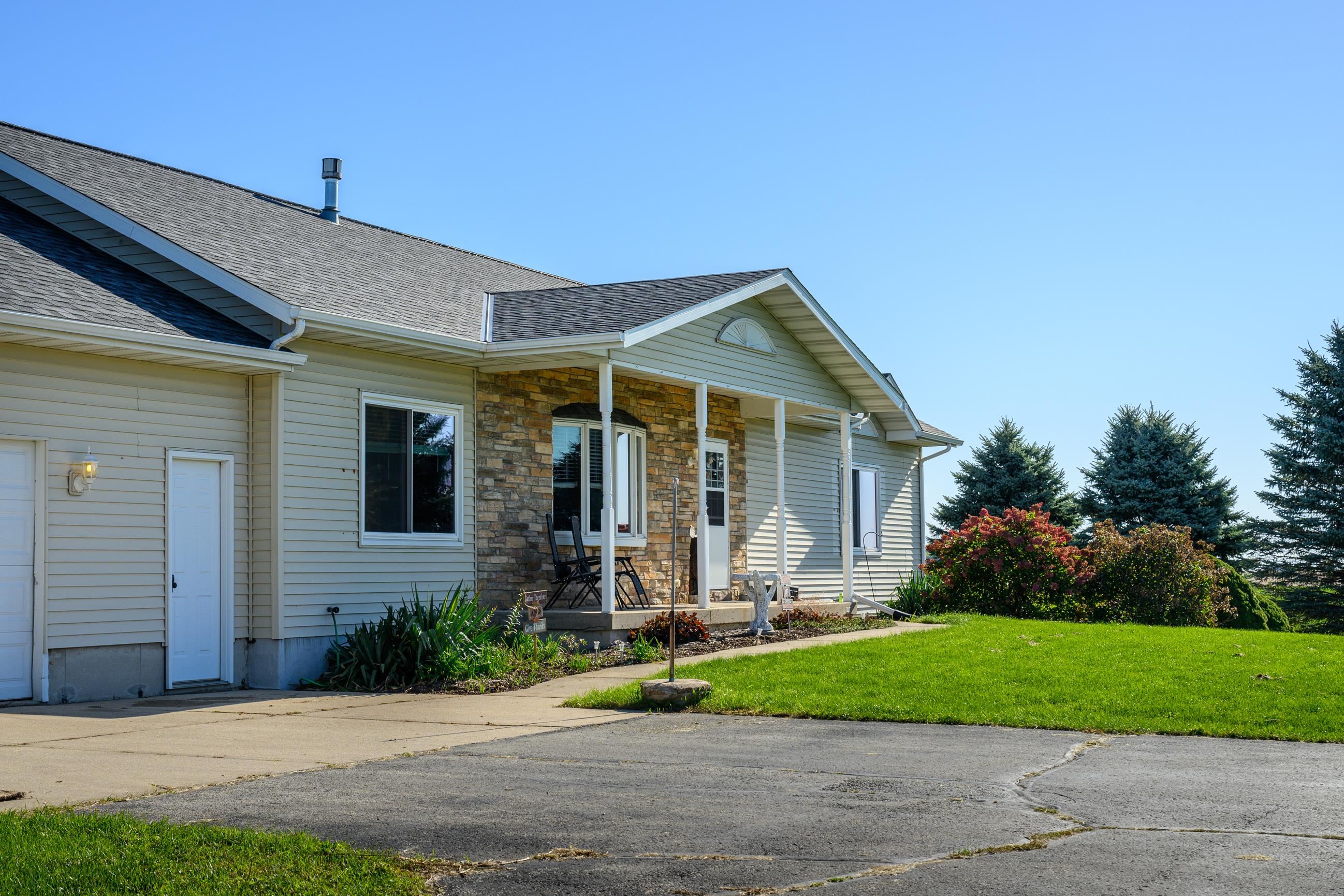 House exterior with a stone-faced covered porch, attached garage, and evergreen landscaping.