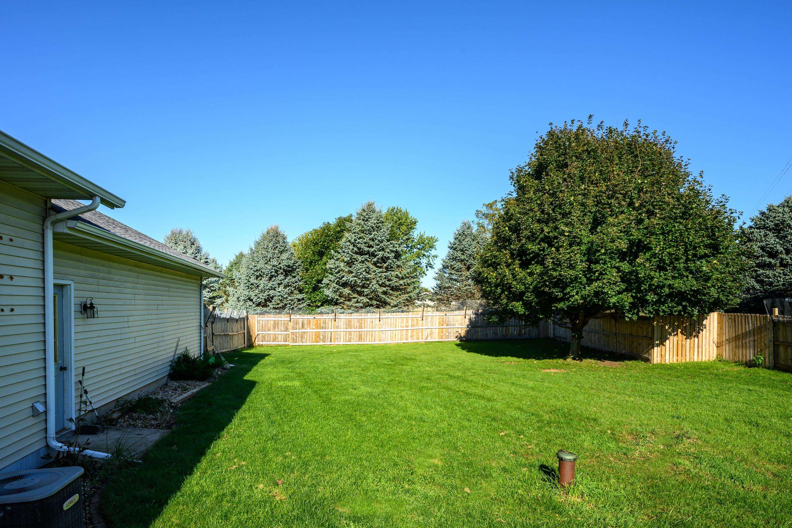 Fenced backyard with a broad lawn, mature shade tree, and the side of the house.
