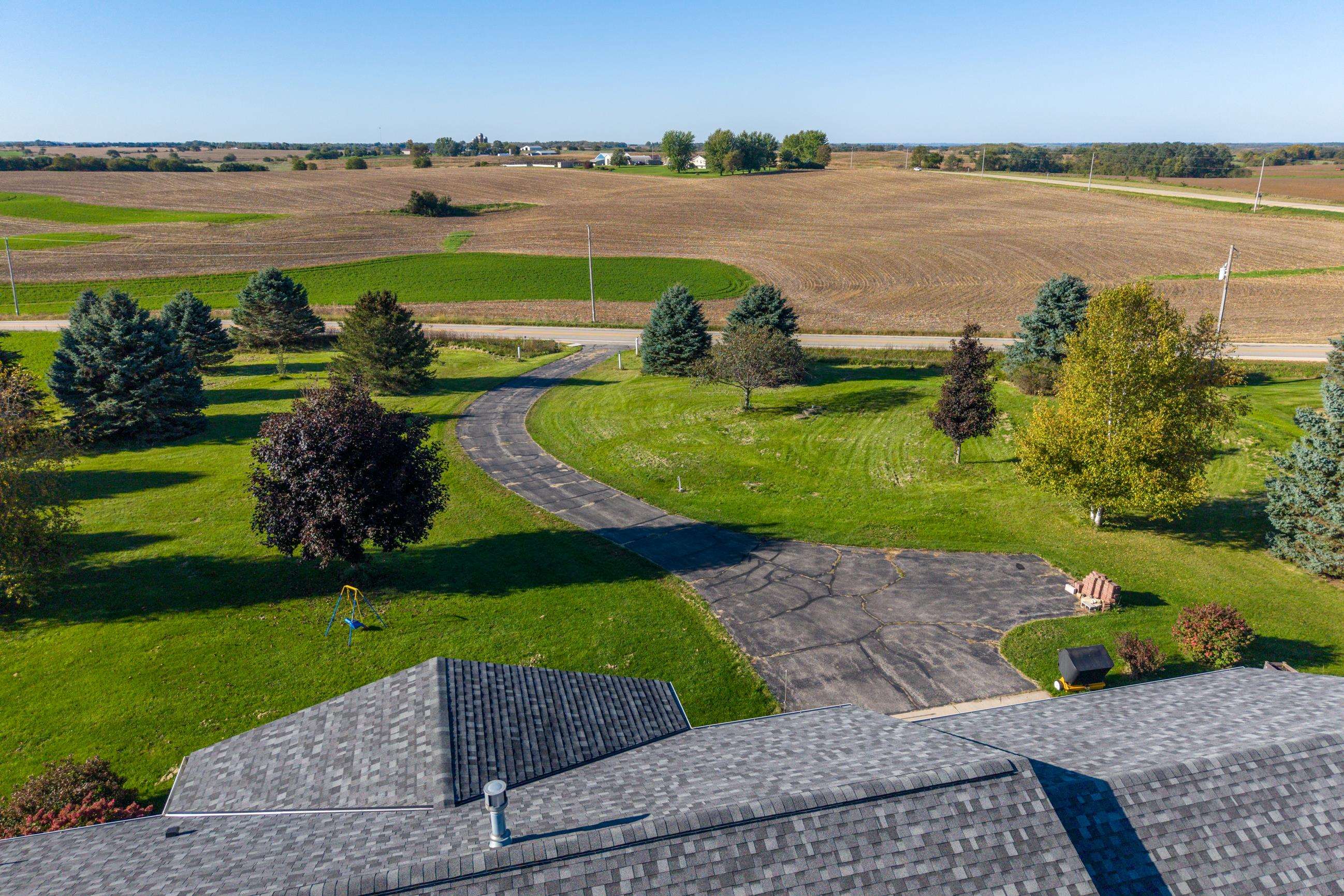Aerial view of a rural property with a curved driveway, landscaped lawn, and surrounding farm fields.