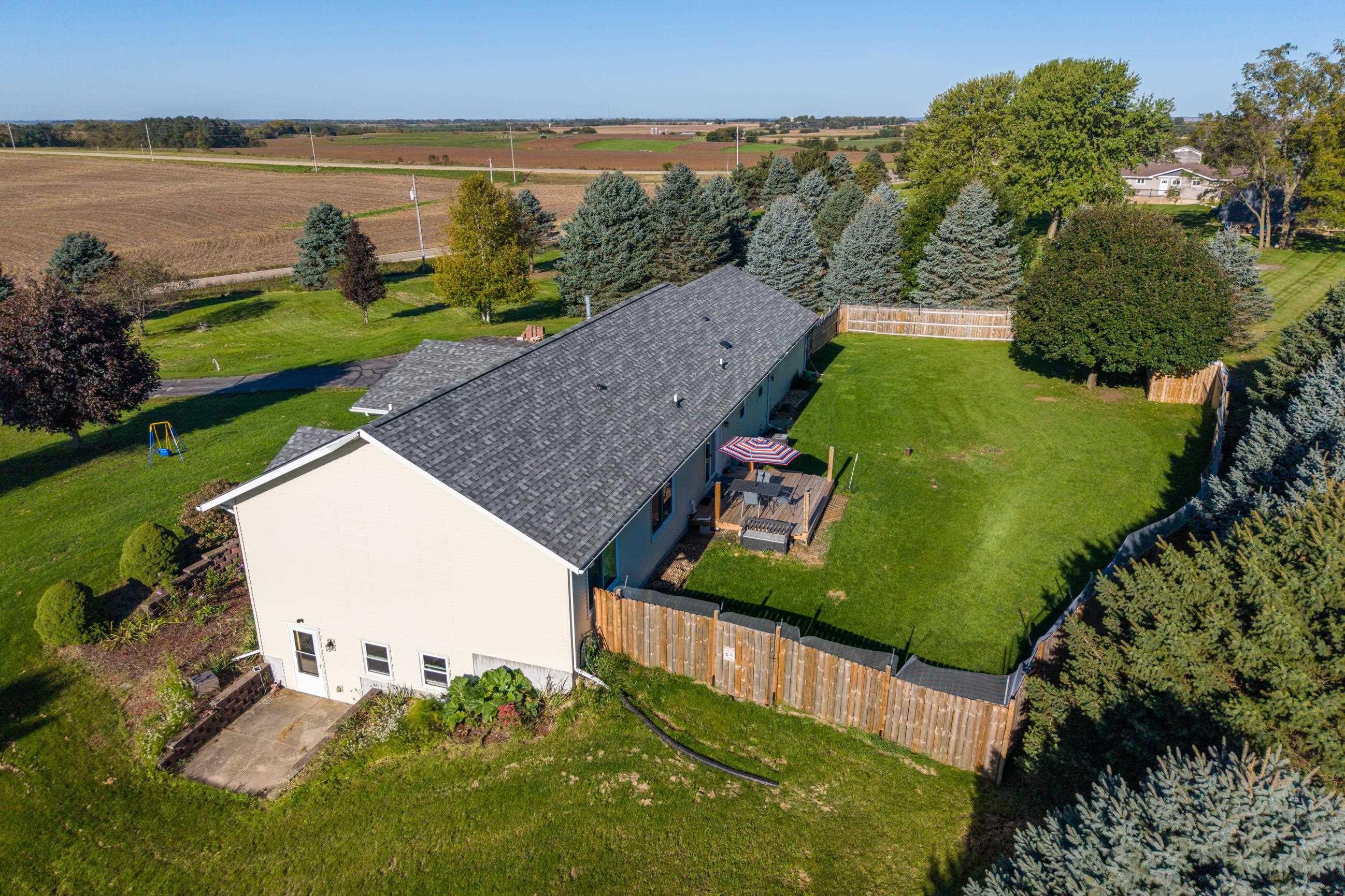 Aerial view of a home with a fenced lawn, deck, and surrounding farmland.