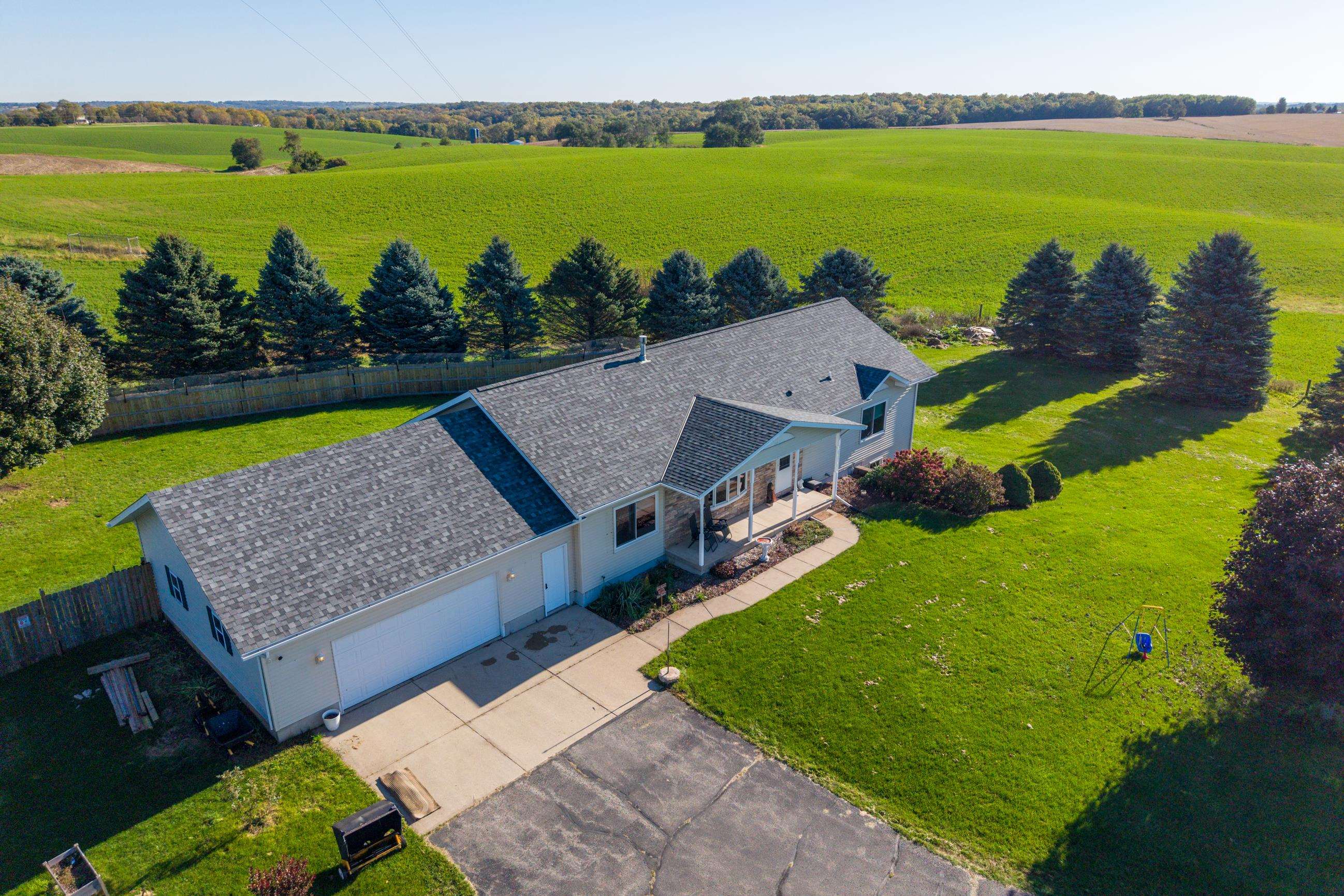 Aerial view of a ranch-style home with a broad lawn, evergreen trees, and surrounding farmland.