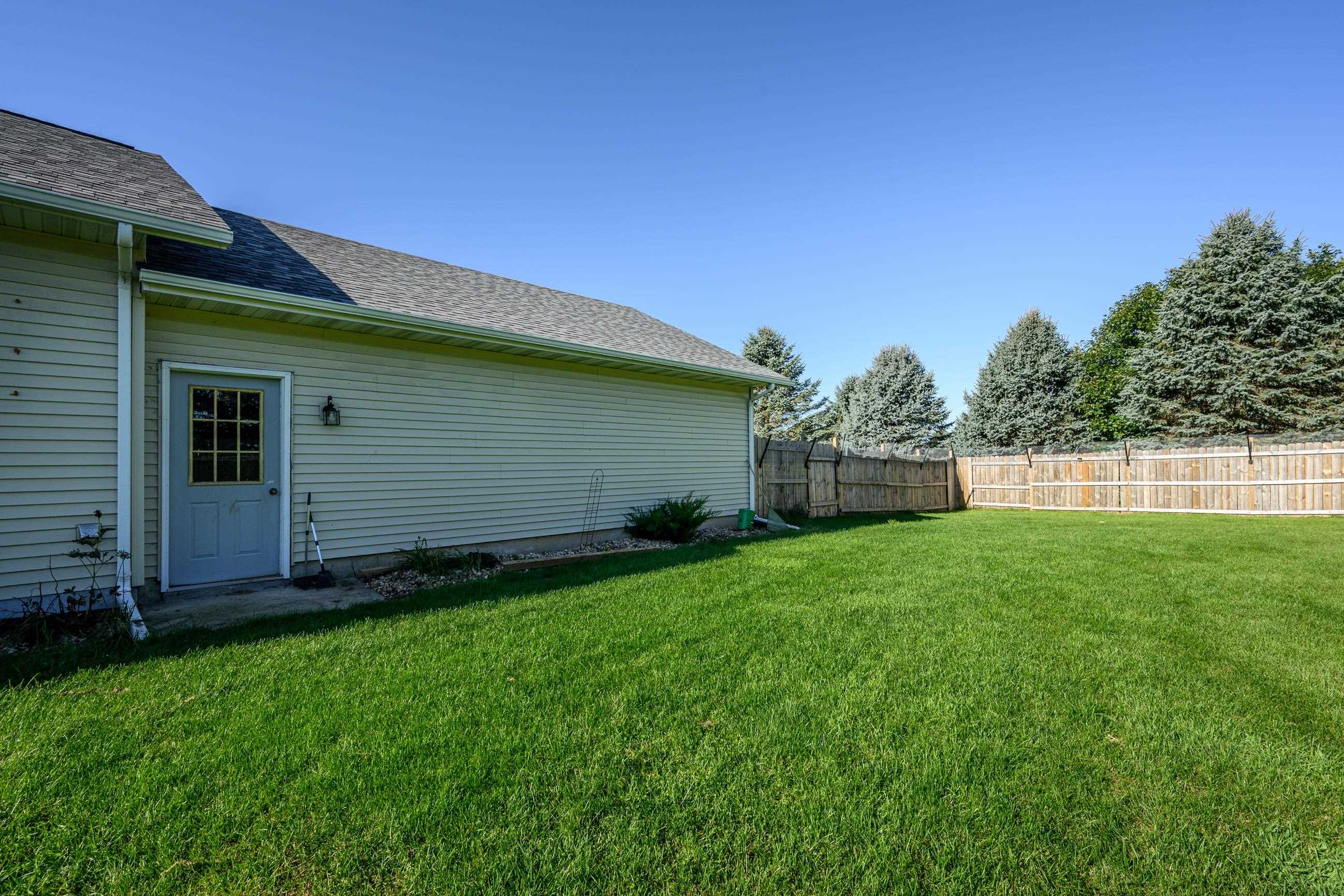 House side entrance beside a broad fenced lawn and mature evergreen trees.