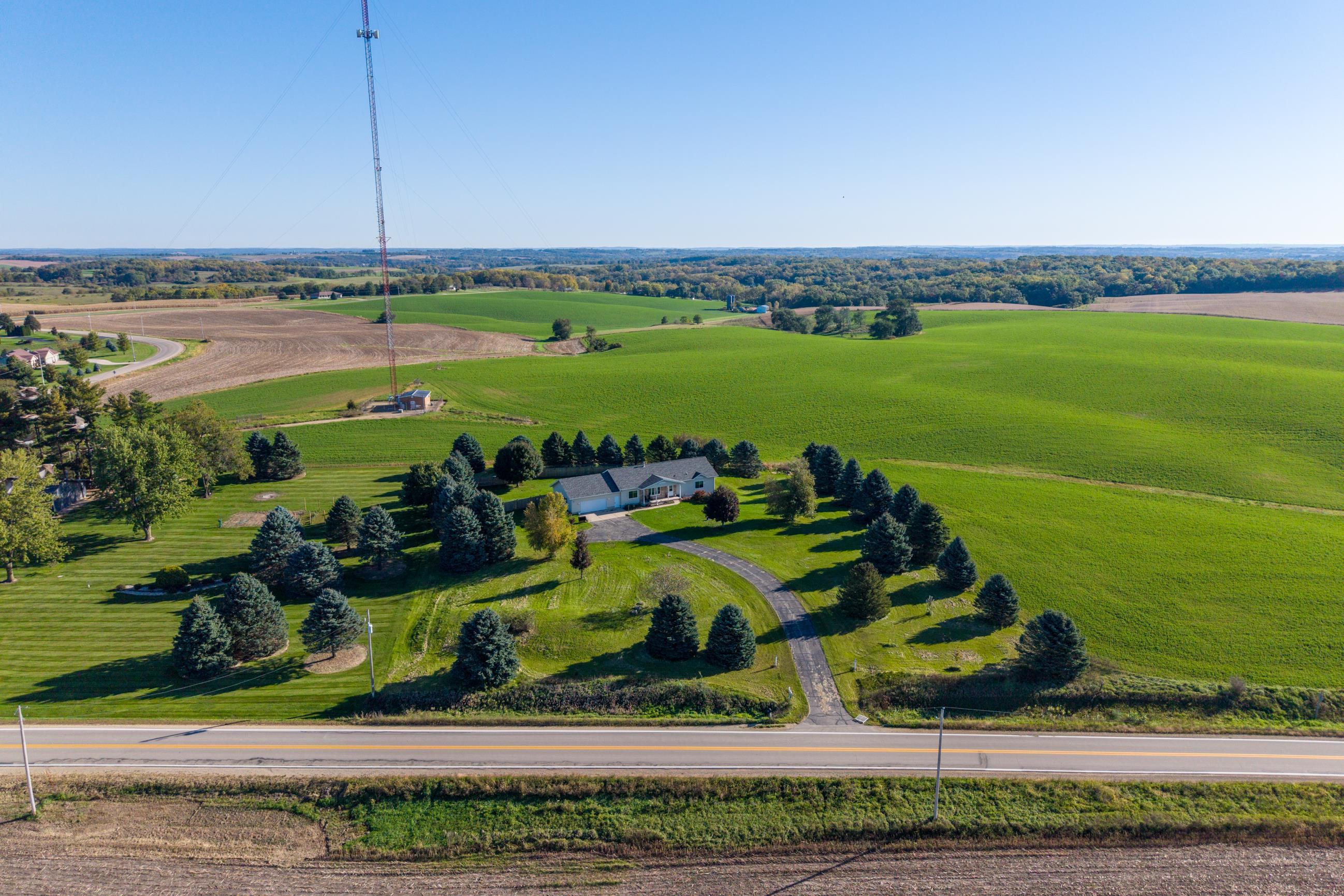 Aerial view of a rural home with a curved driveway, mature evergreens, and surrounding farmland.