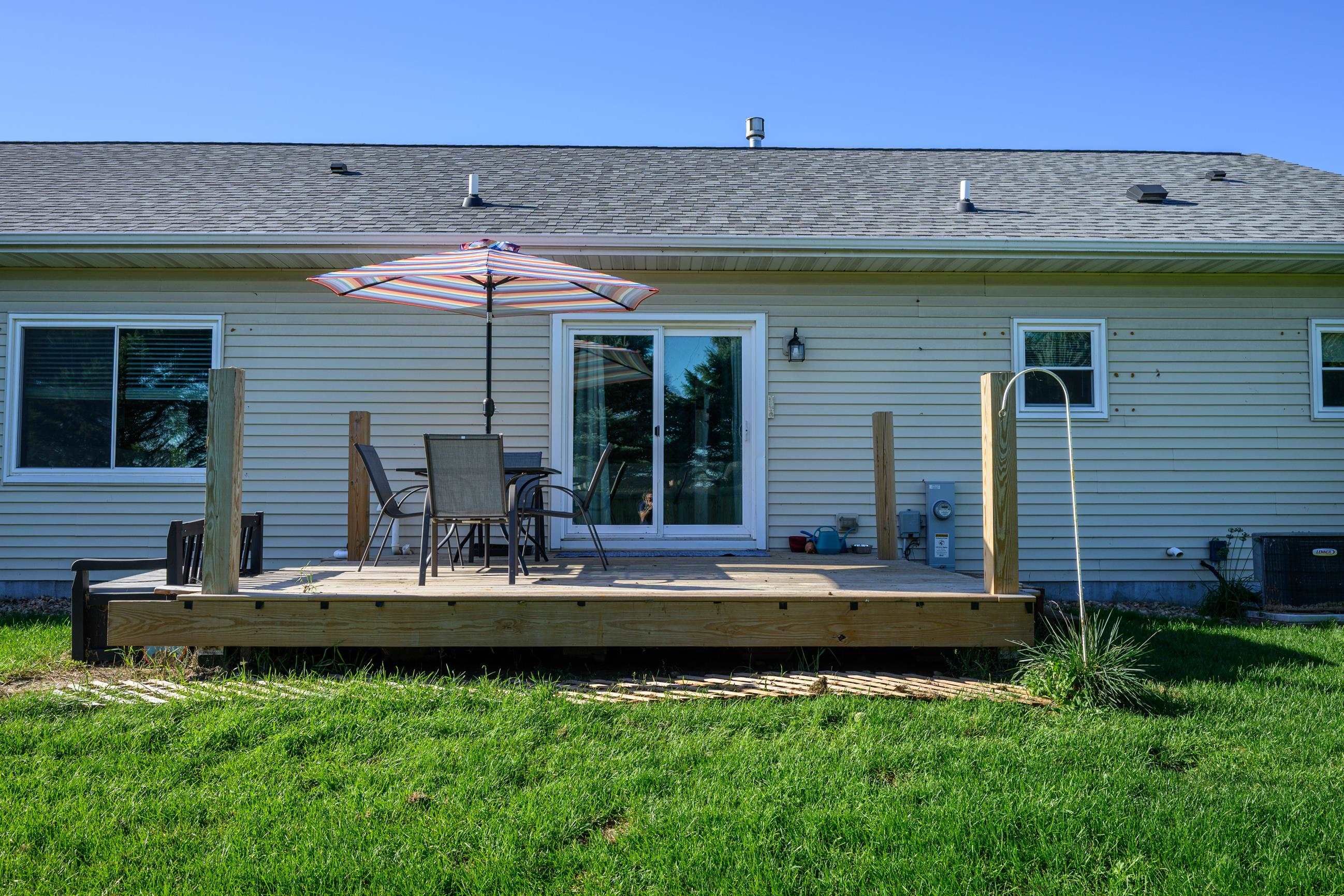 Rear of a light-sided home with a raised wooden deck, patio furniture, and striped umbrella.