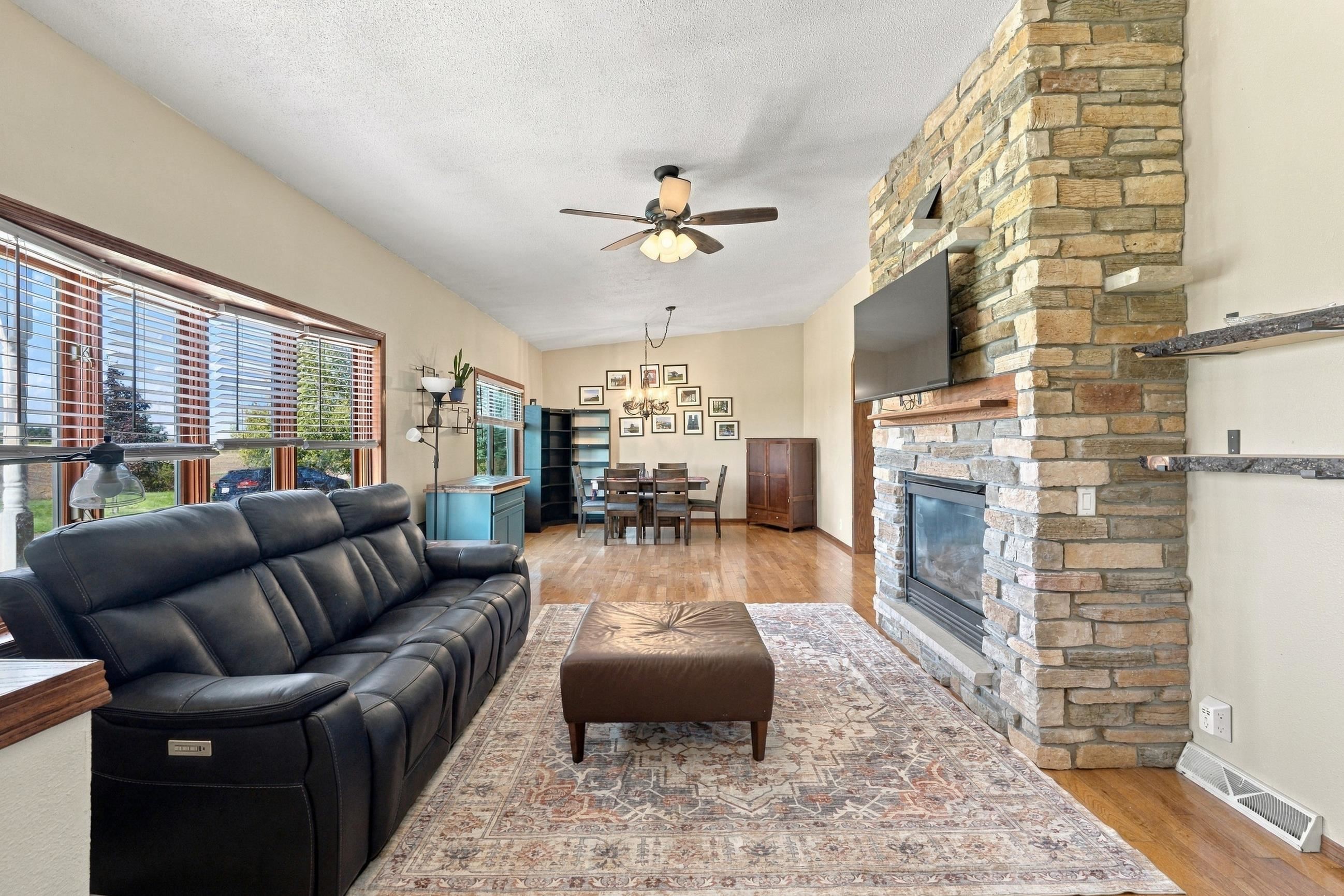 Living room with a floor-to-ceiling stone fireplace, black leather sofa, and dining area beyond.