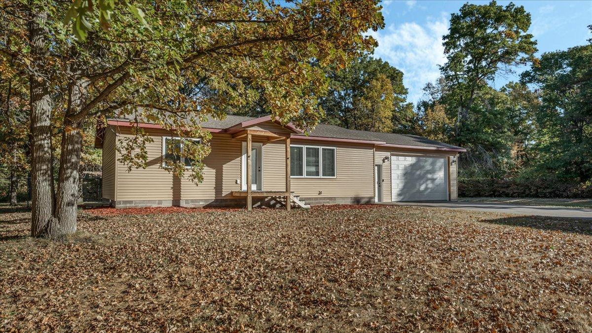 Tan single-story home with attached garage beneath mature trees and autumn leaves.