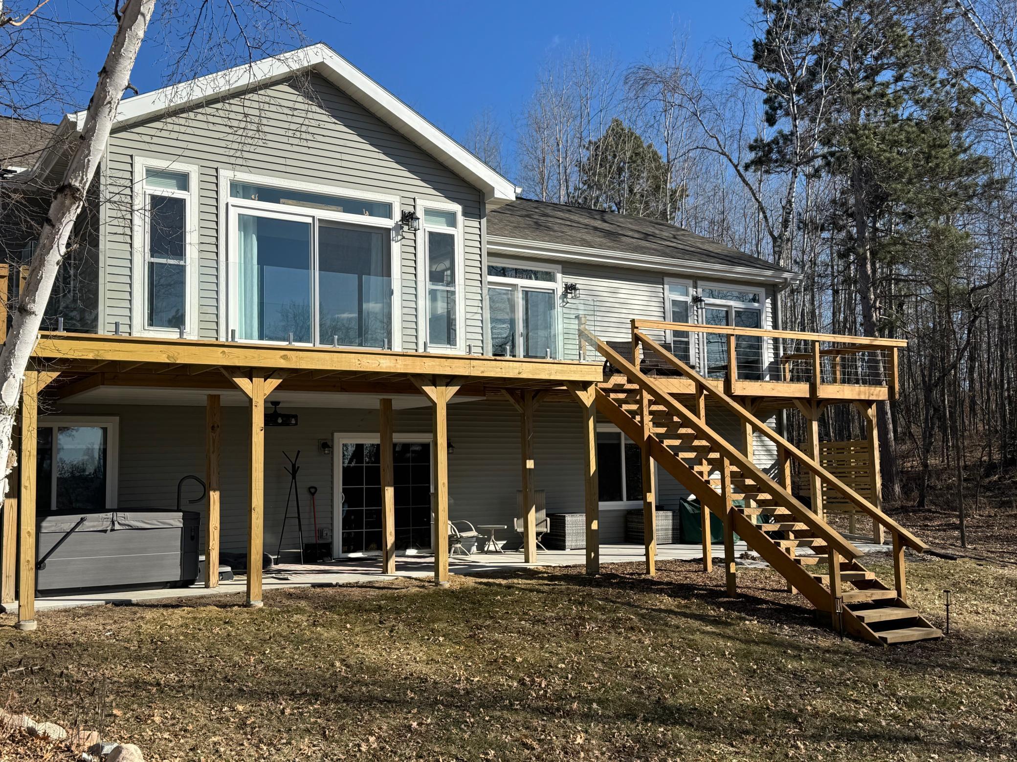 Home with a raised wooden deck, long staircase, and hot tub beneath it, set among leafless trees.