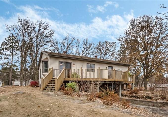 Light-colored home with a long raised wooden deck and stairs among mature trees.