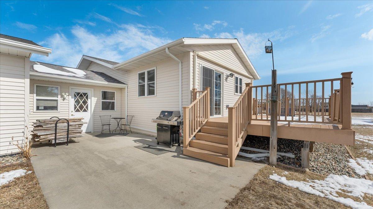 Home’s rear patio and raised deck with wooden stairs, a grill, and patches of snow.